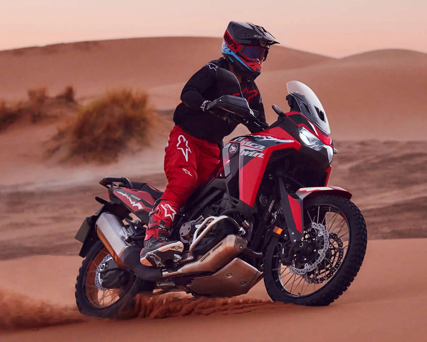 Rider in red and black gear on a red and black Honda Africa Twin motorcycle riding on sand dunes.