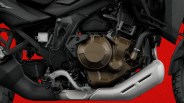 Close-up of a motorcycle engine with bronze casing and silver exhaust pipe against a red background.