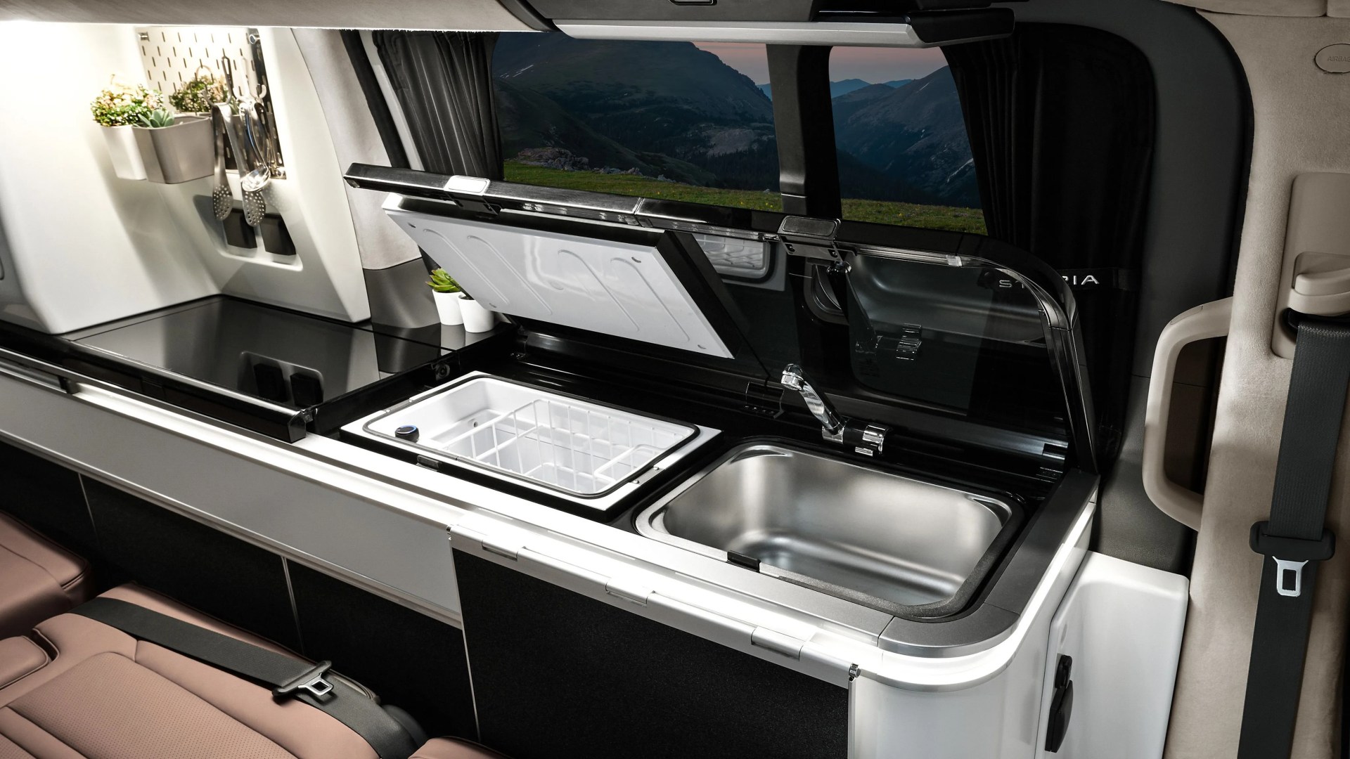Compact campervan kitchen with a stainless steel sink, small fridge, induction cooktop, and hanging utensils.