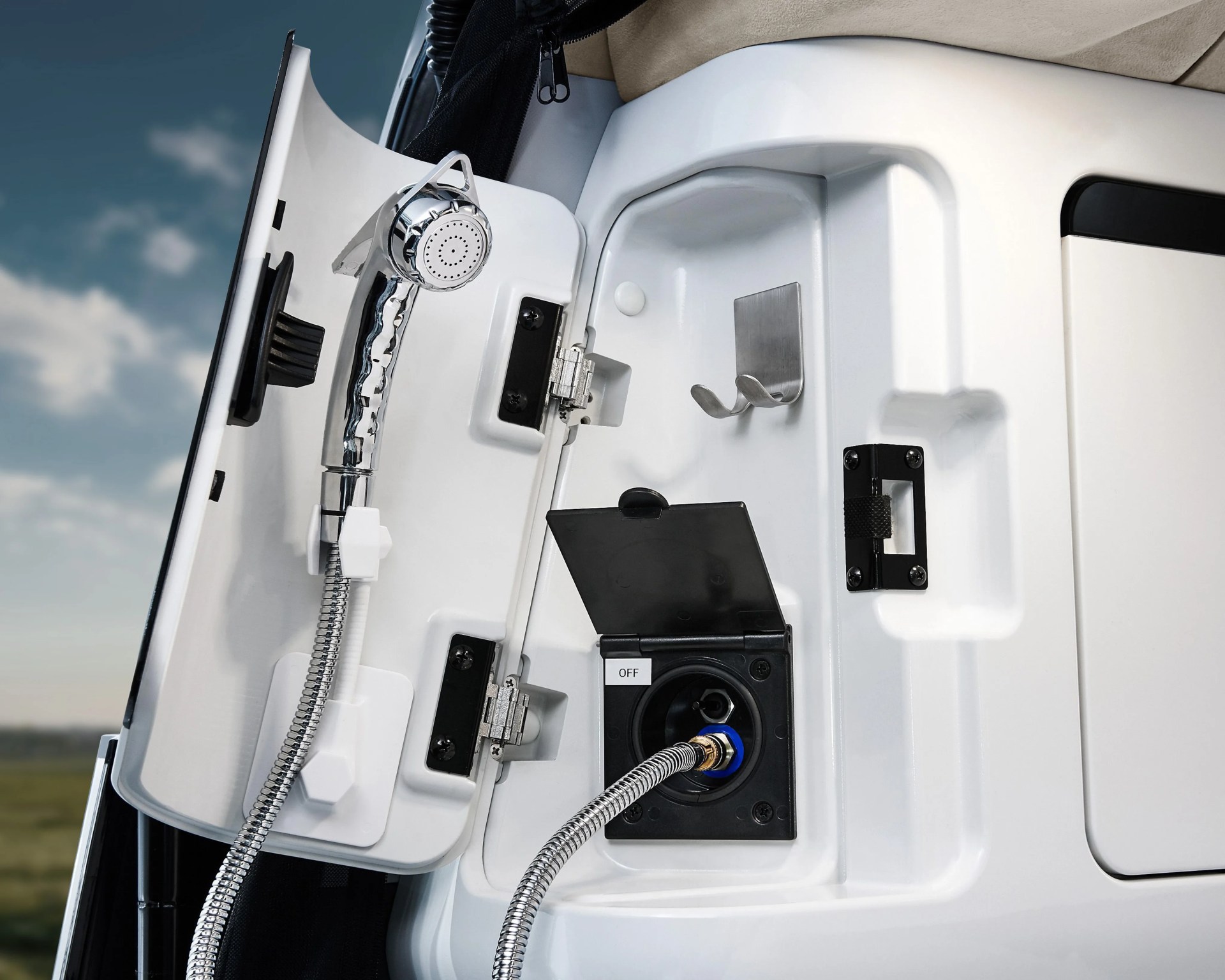 White outdoor shower compartment with chrome handheld showerhead and flexible hose attached to a black water outlet panel.