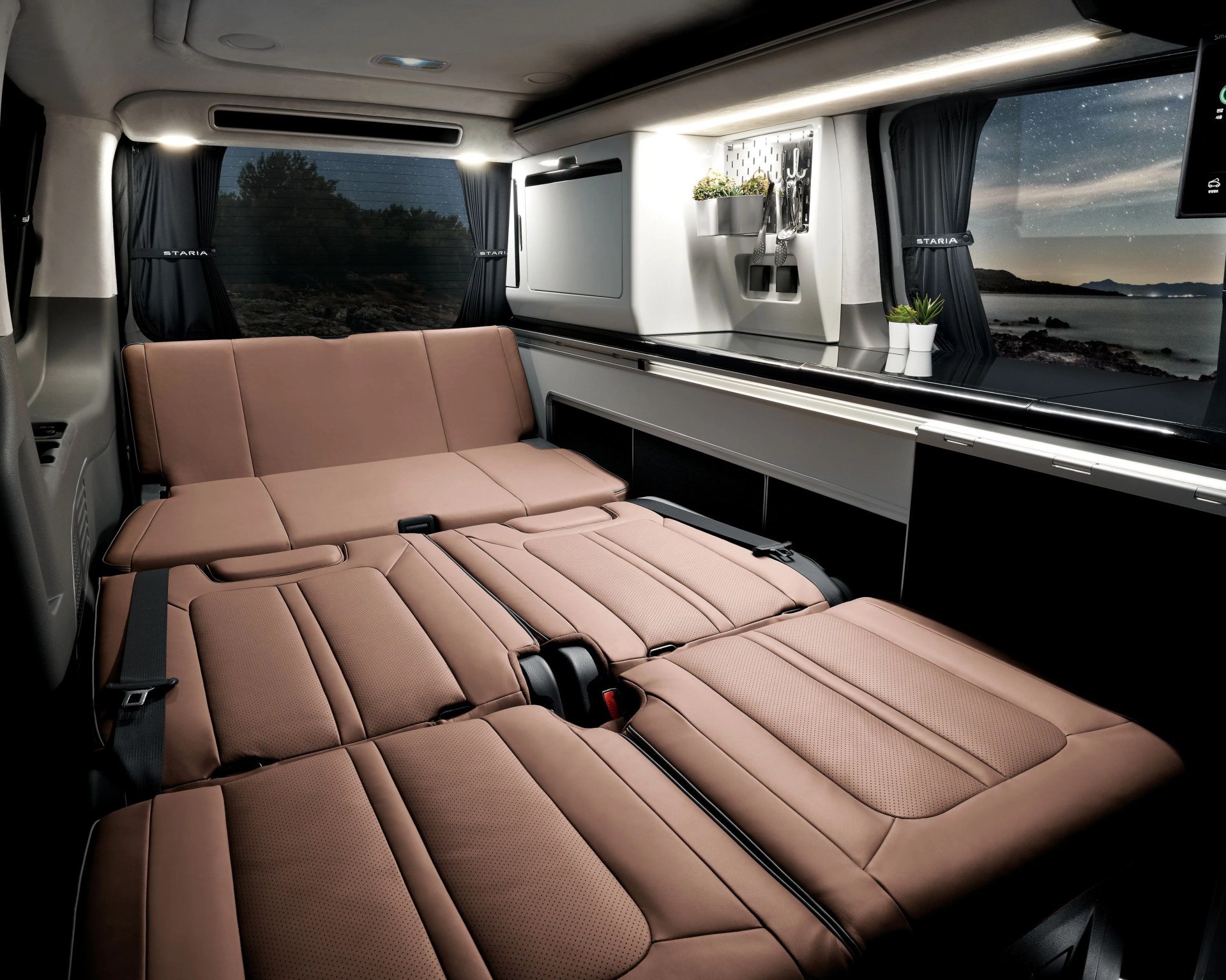 Brown leather fold-out bed inside a camper van with black curtains and a kitchenette area.