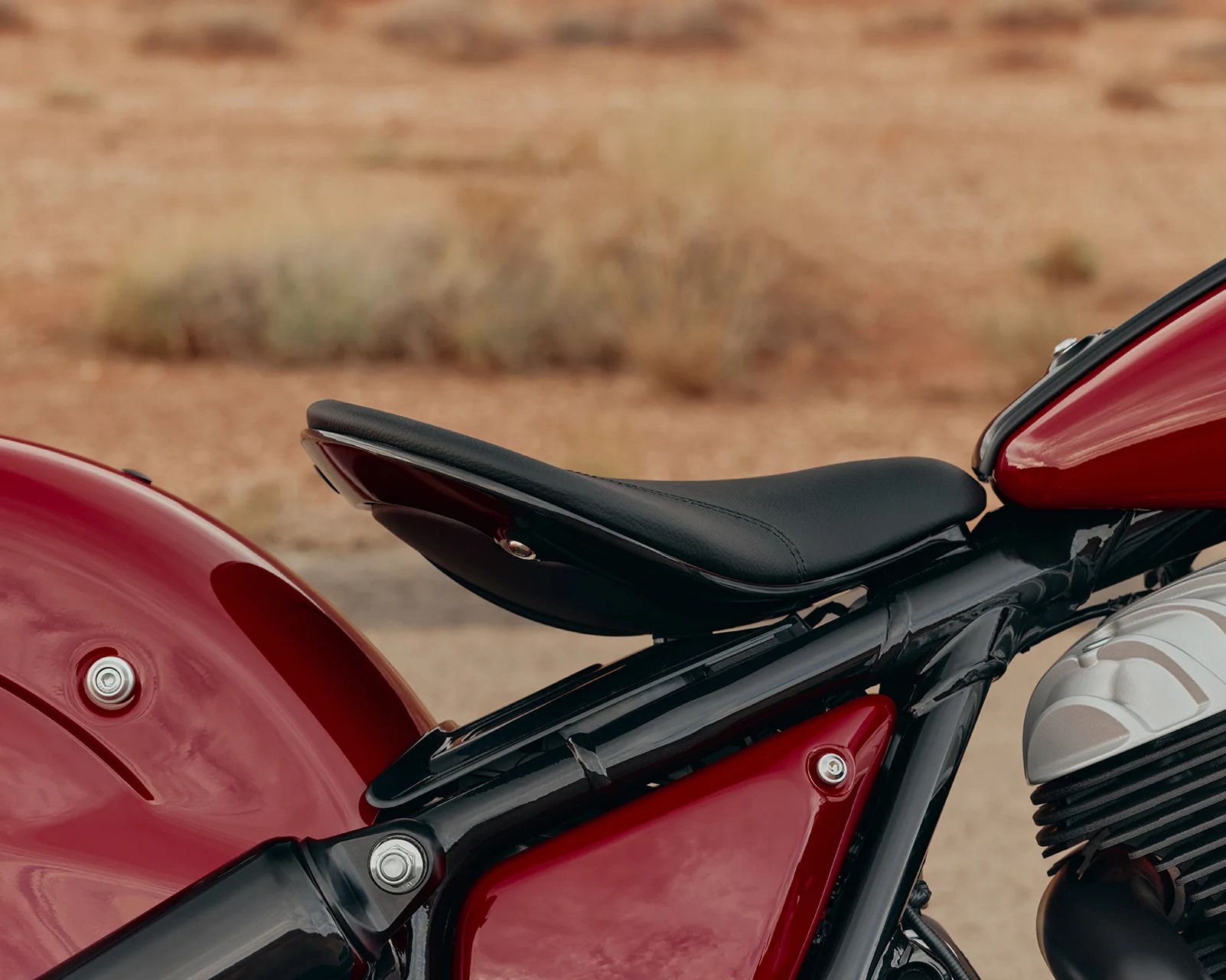 Black leather solo motorcycle seat mounted on a black frame with red body panels.