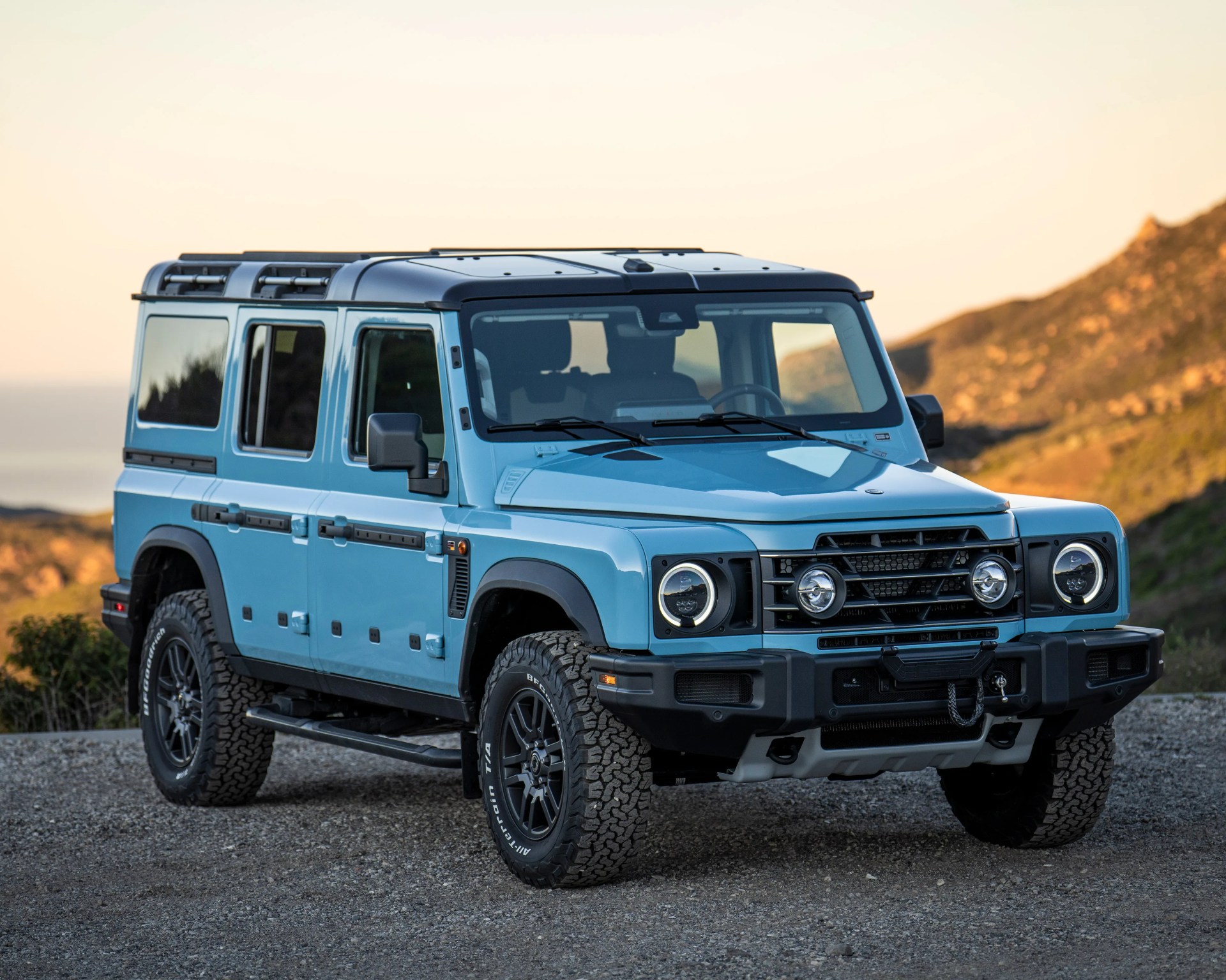 Light blue four-door off-road SUV with black roof and rugged tires parked on gravel with hills in the background.