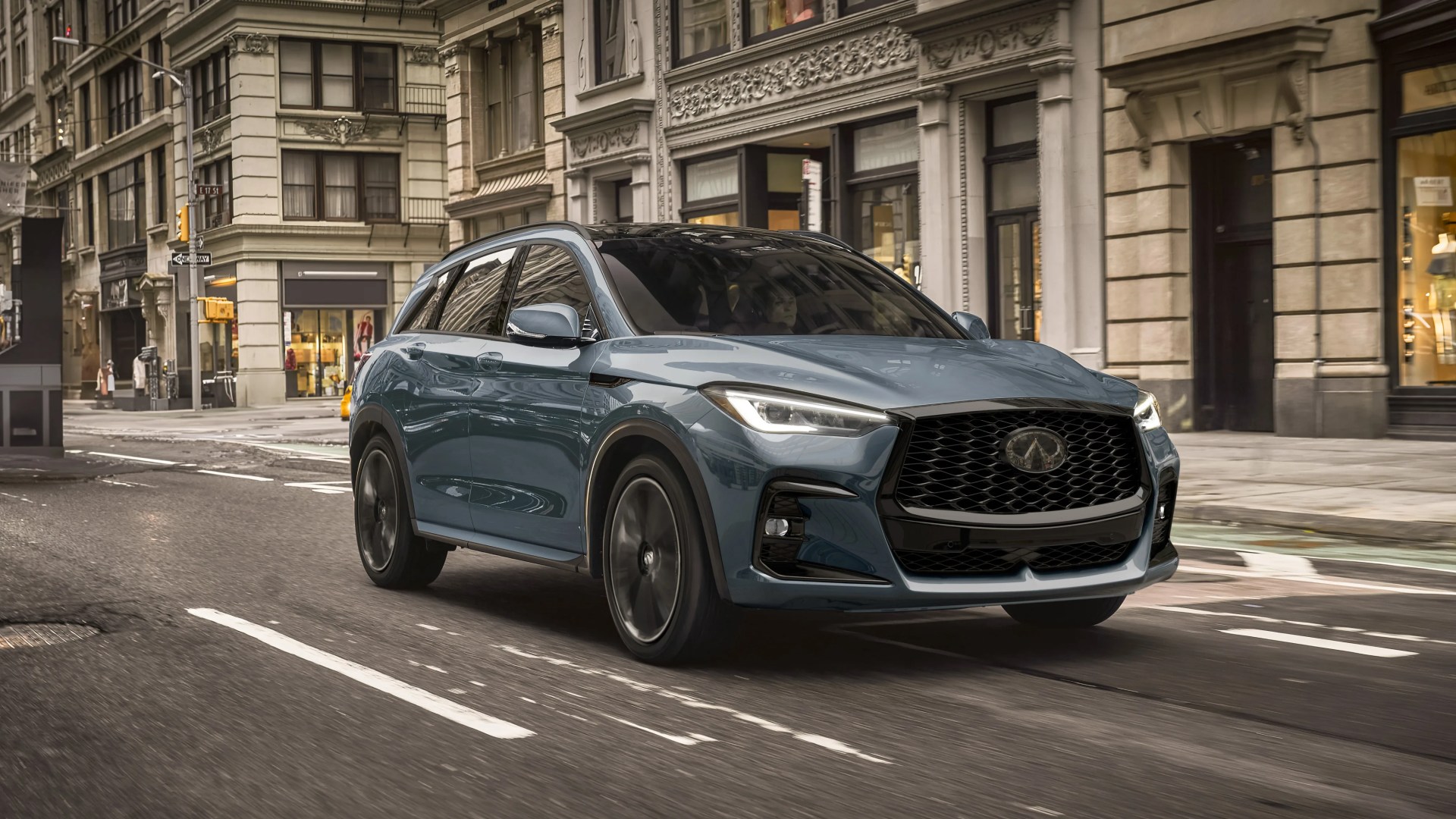 Blue Infiniti SUV with black grille and wheels driving on a city street.