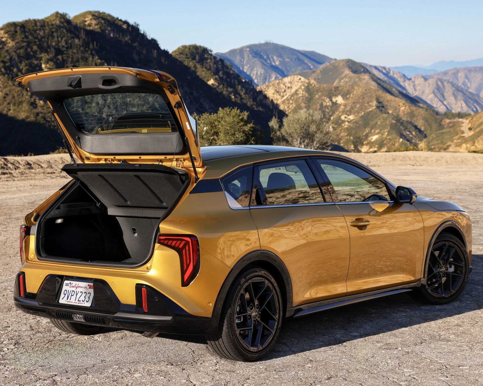 Gold crossover SUV with open rear hatch parked on a mountain road with rugged hills in the background.