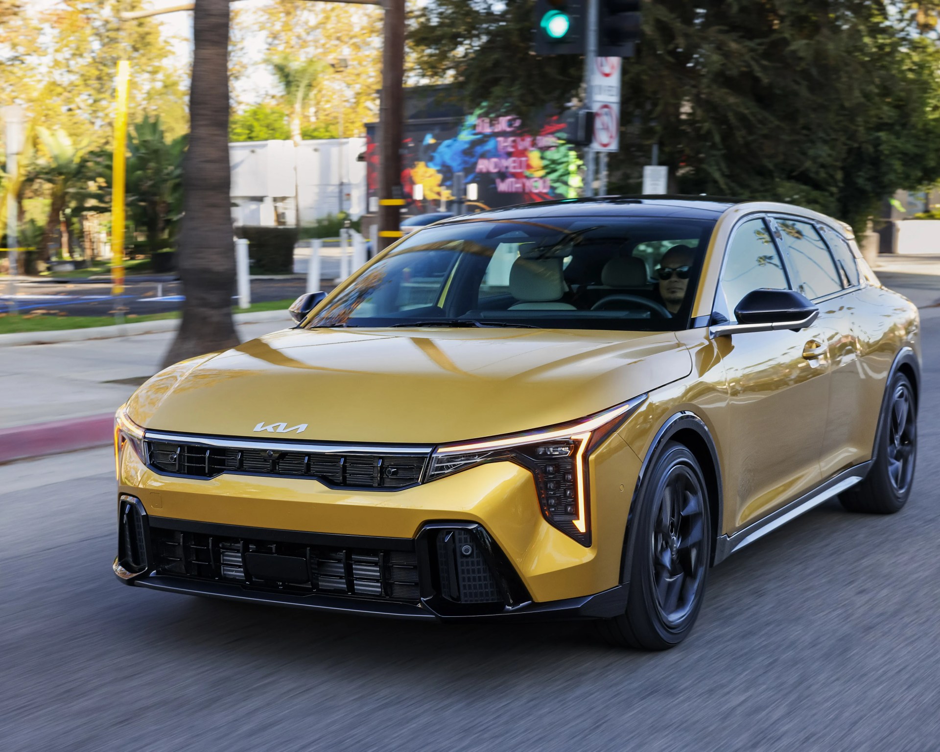 Yellow Kia electric sedan with black roof and wheels driving on a city street.