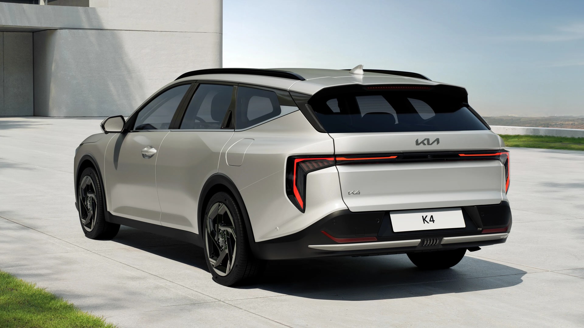 Silver Kia K4 SUV with black roof rails and angular rear LED lights parked on a concrete surface.