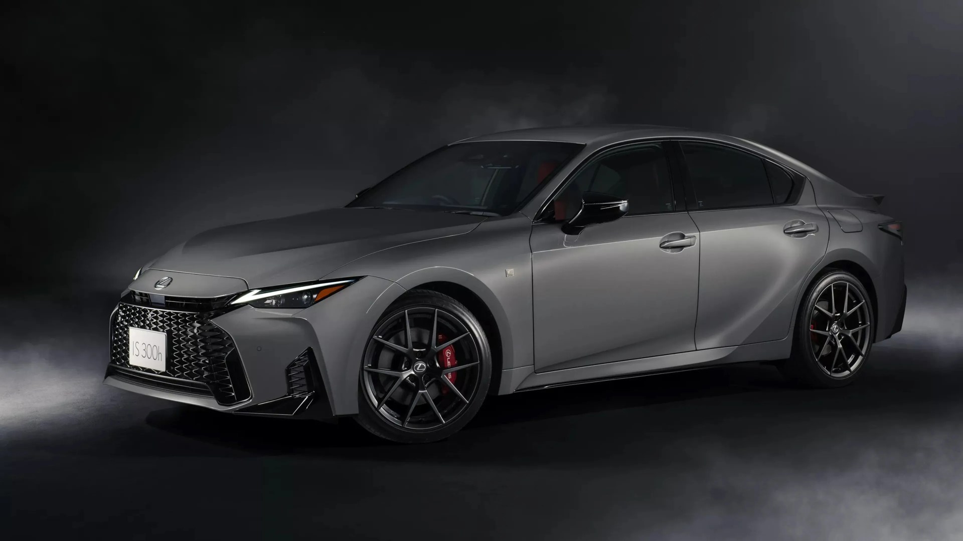 Matte gray Lexus IS 300h sedan with black wheels and red brake calipers in a dark smoky setting.