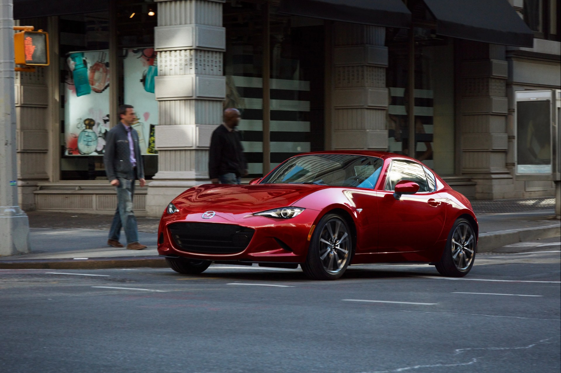 Shiny red Mazda MX-5 Miata sports car parked on a city street near a crosswalk.