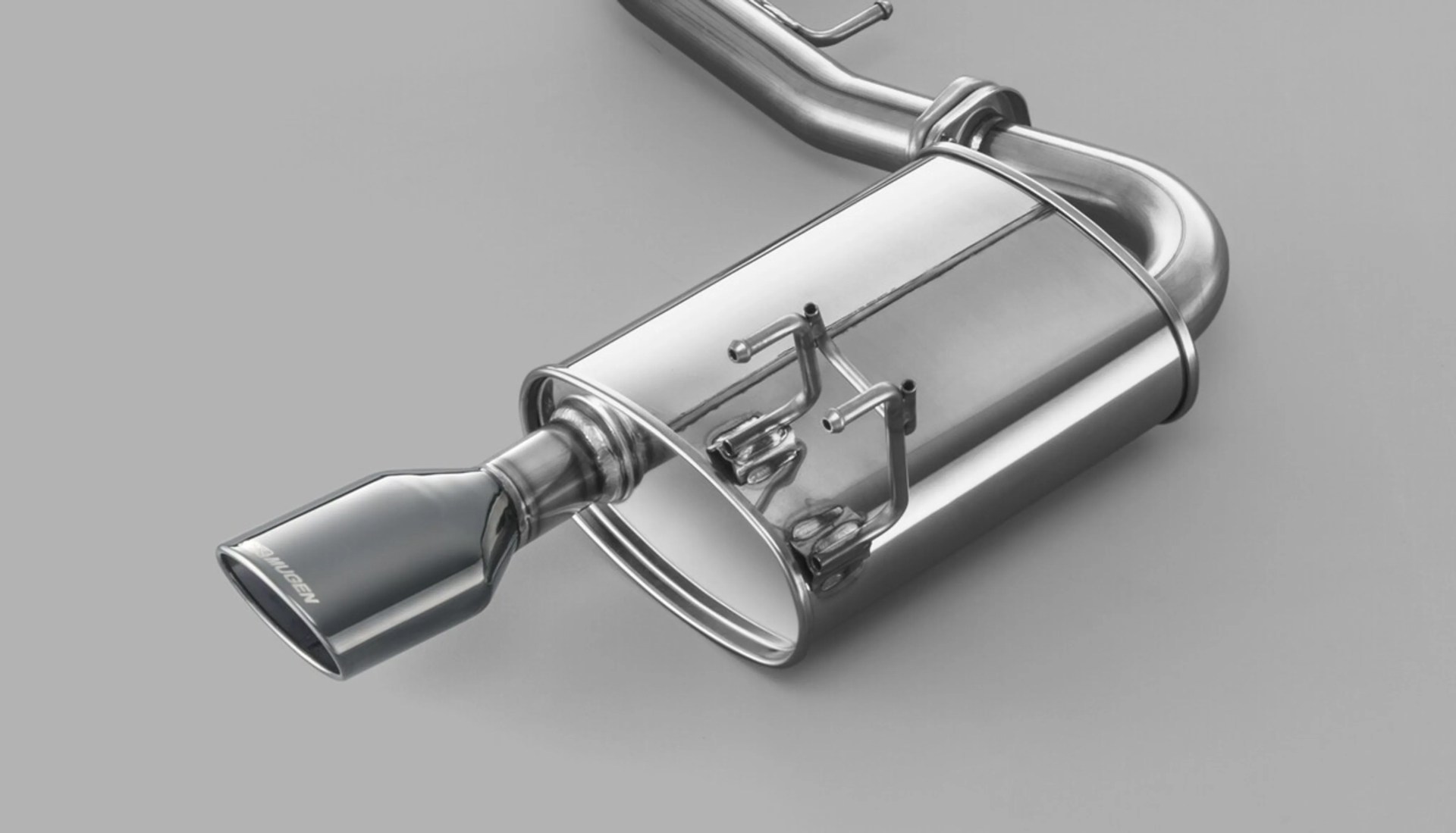 Polished stainless steel car exhaust muffler with a black Mugen-branded tip on a gray surface.