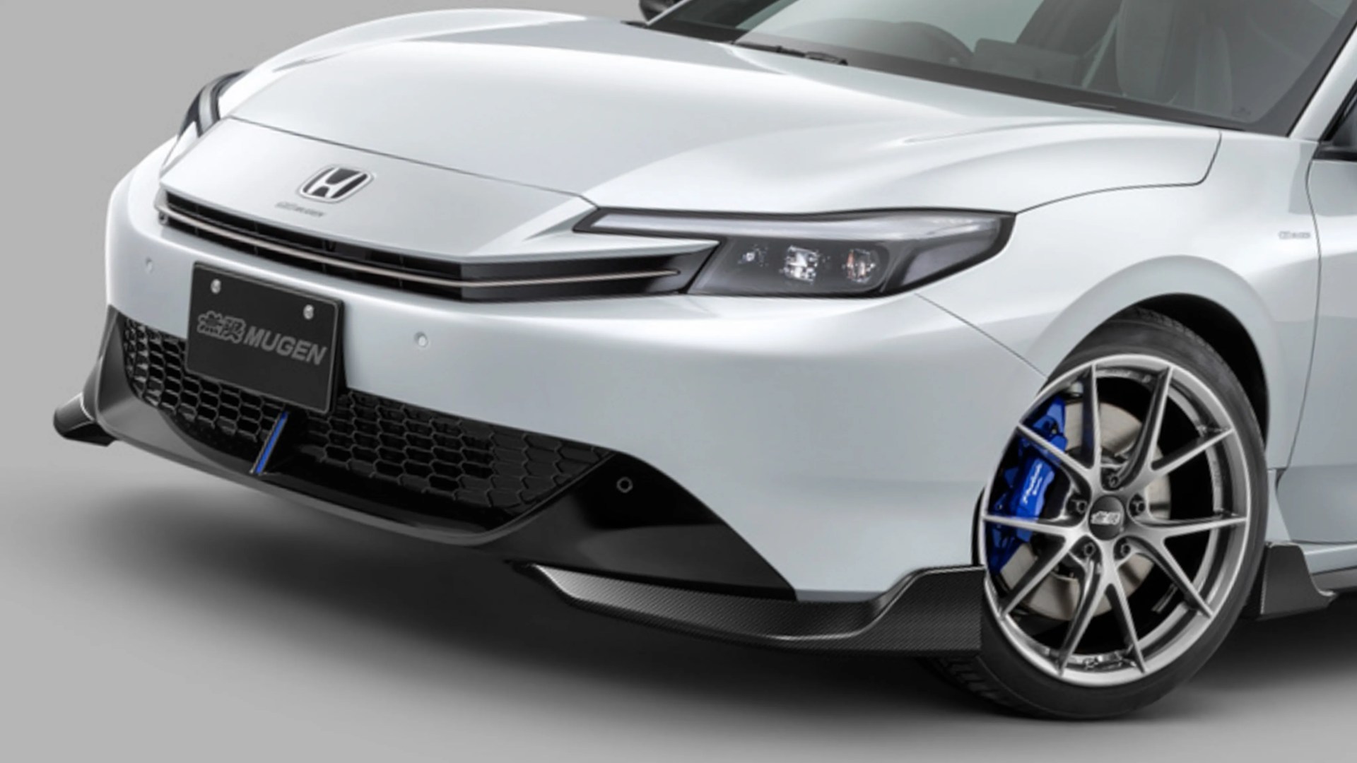 Front view of a white Honda car with Mugen license plate, black grille, blue brake calipers, and silver alloy wheels.