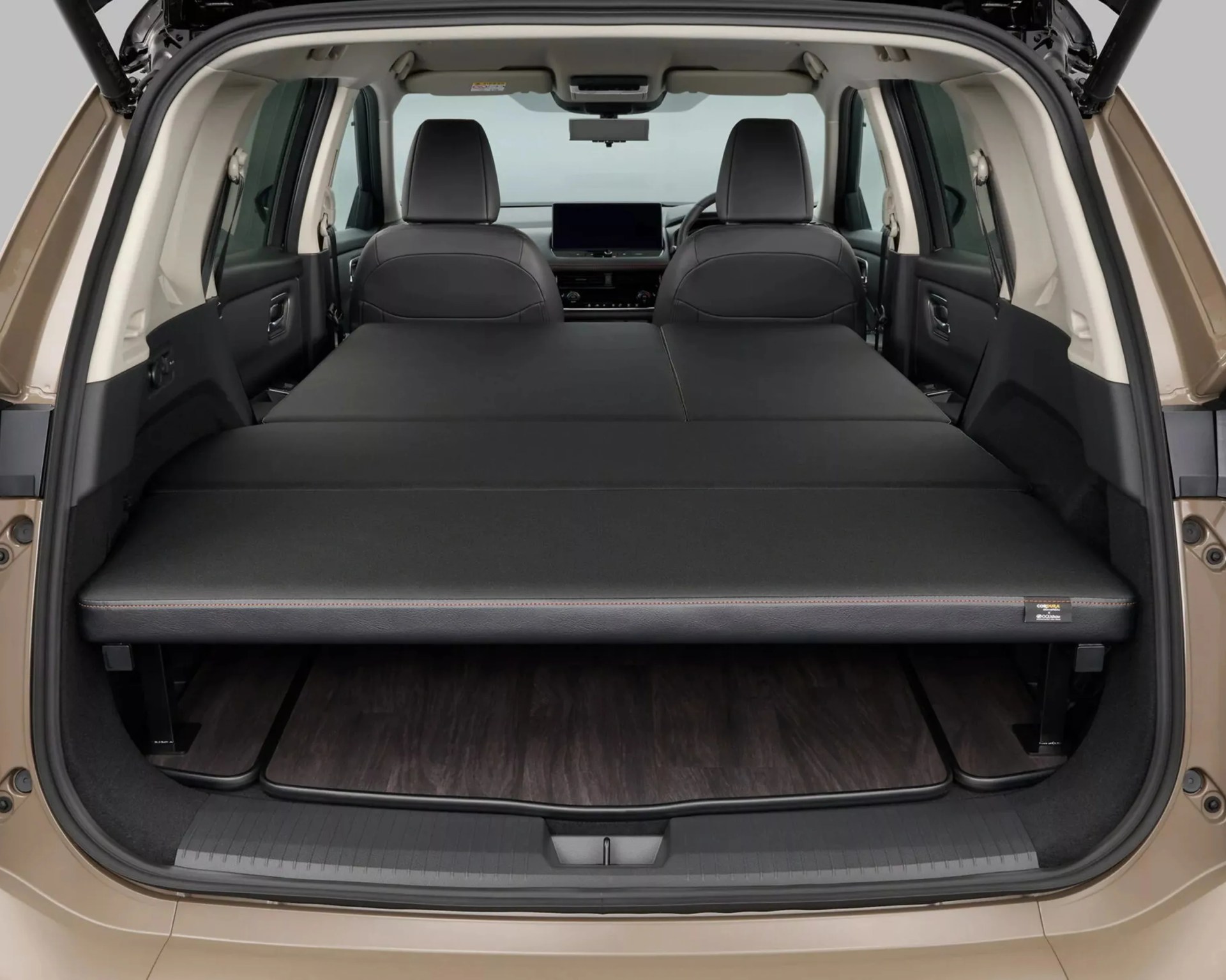 Flat black foldable mattress laid out in the rear cargo area of a beige SUV with front seats visible.