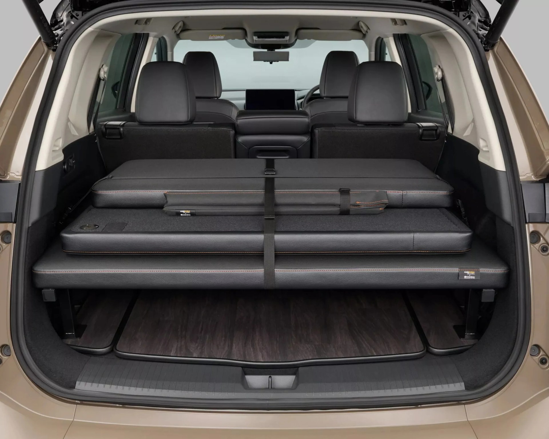Rear cargo area of a beige SUV with a folded black leather multi-layered mattress or cushion secured with straps.