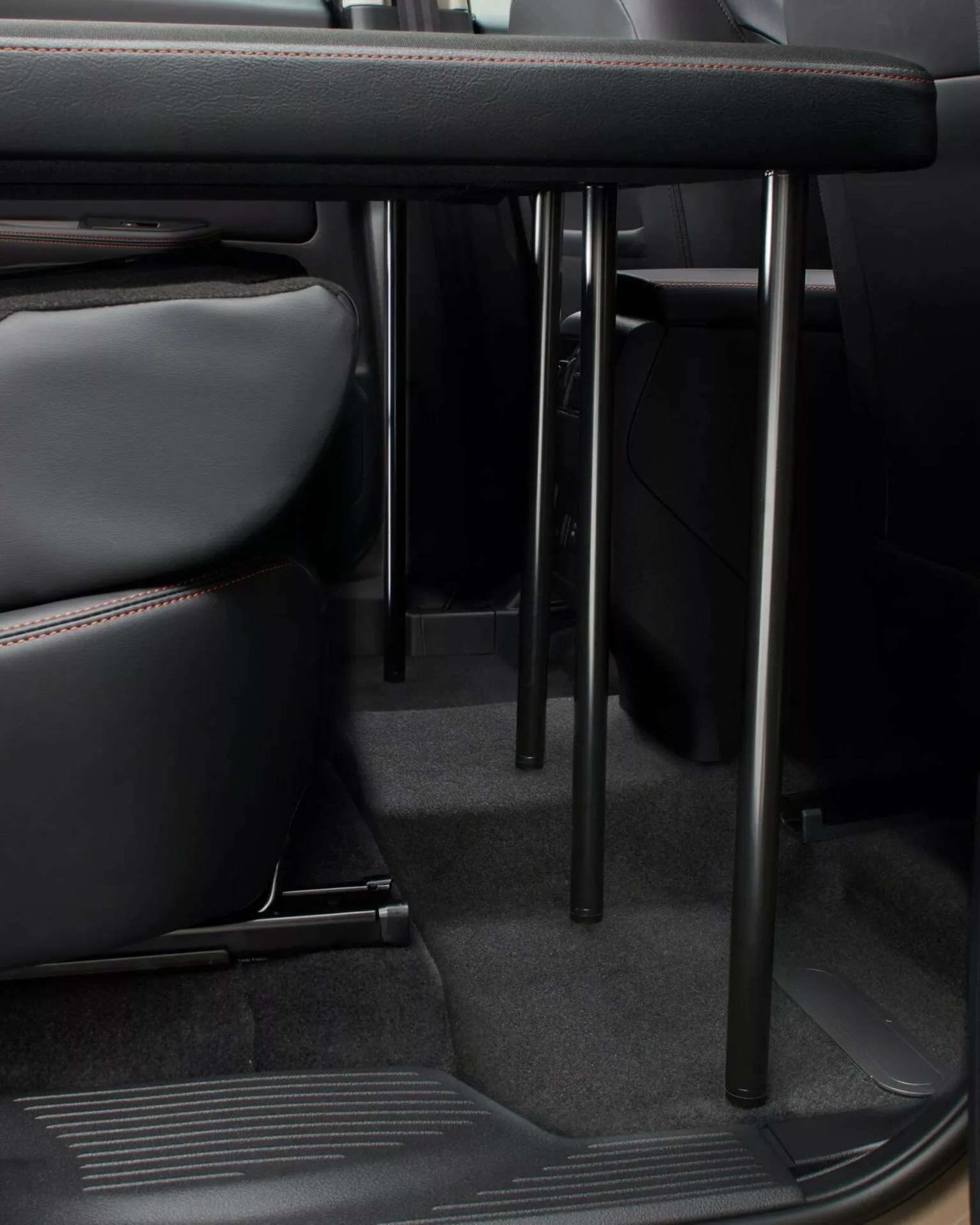 Black metal table legs attached to a black leather surface inside a vehicle between two seats.
