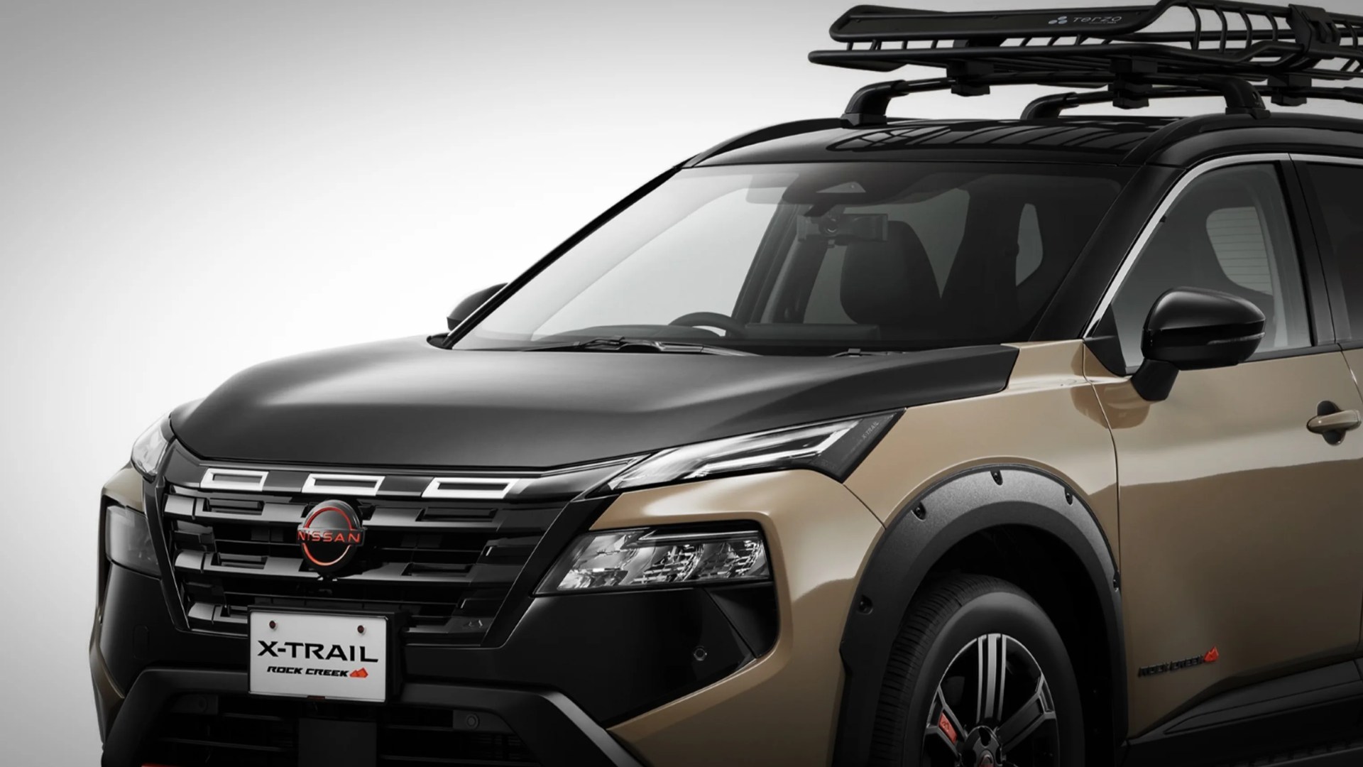 Front side view of a beige and black Nissan X-Trail Rock Creek edition SUV with roof rack and black fender flares.