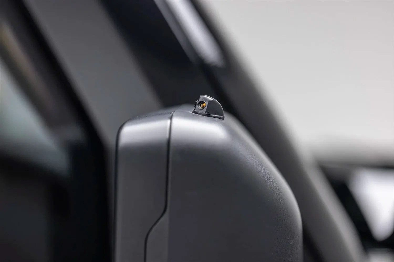 Close-up of a small camera mounted on the top edge of a black car side mirror housing.
