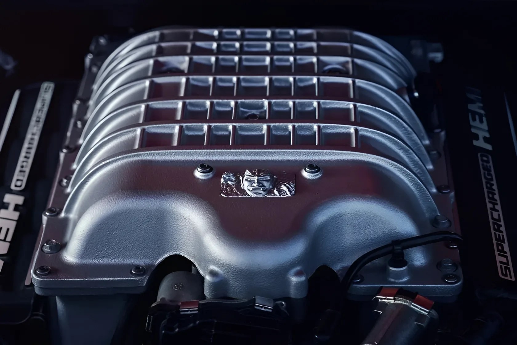 Silver supercharged HEMI engine intake manifold with a Hellcat emblem in a car engine bay.