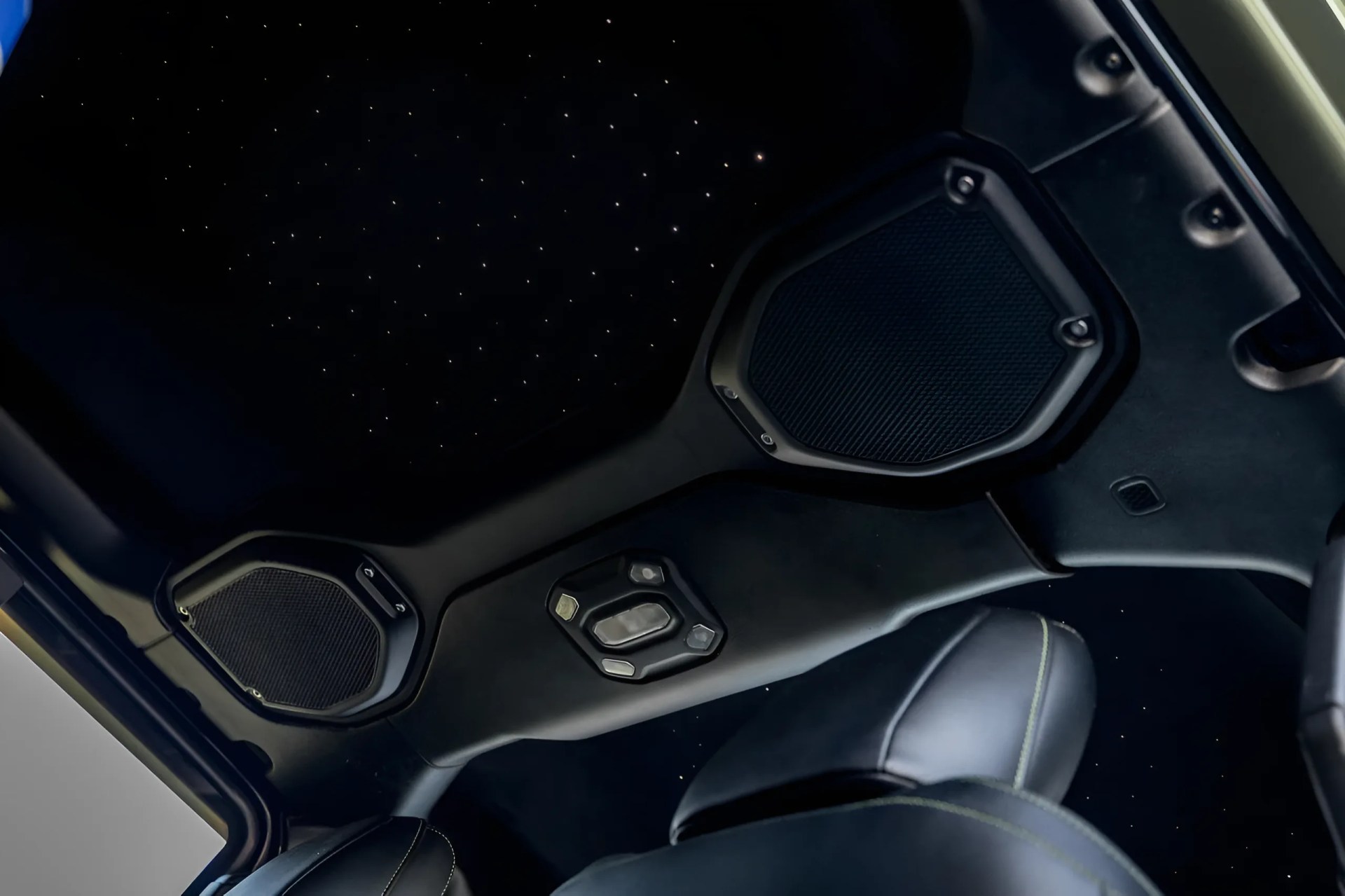 Black car interior ceiling with star-like LED lights and two hexagonal speakers.