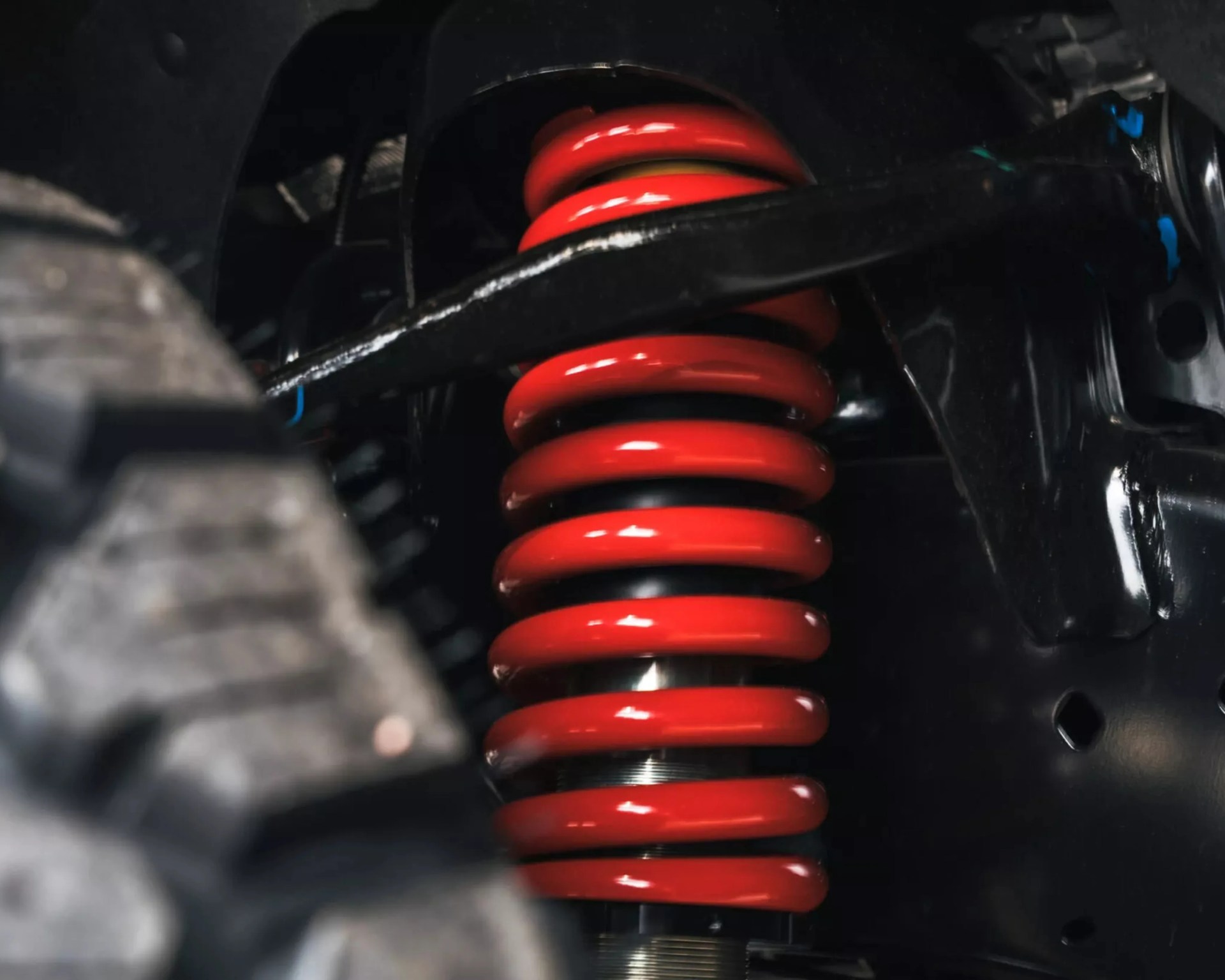 Close-up of a red coil spring suspension system inside a vehicle wheel well.
