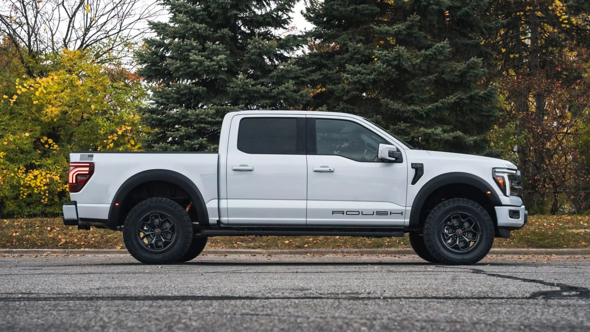 White Roush pickup truck with black wheels parked on a road with trees in the background.