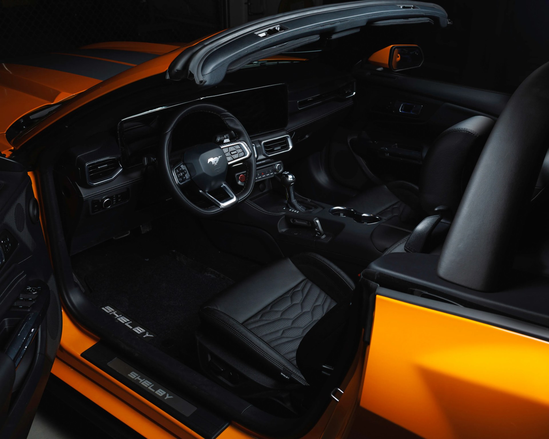 Black leather interior of an orange Shelby convertible with a Mustang logo on the steering wheel.