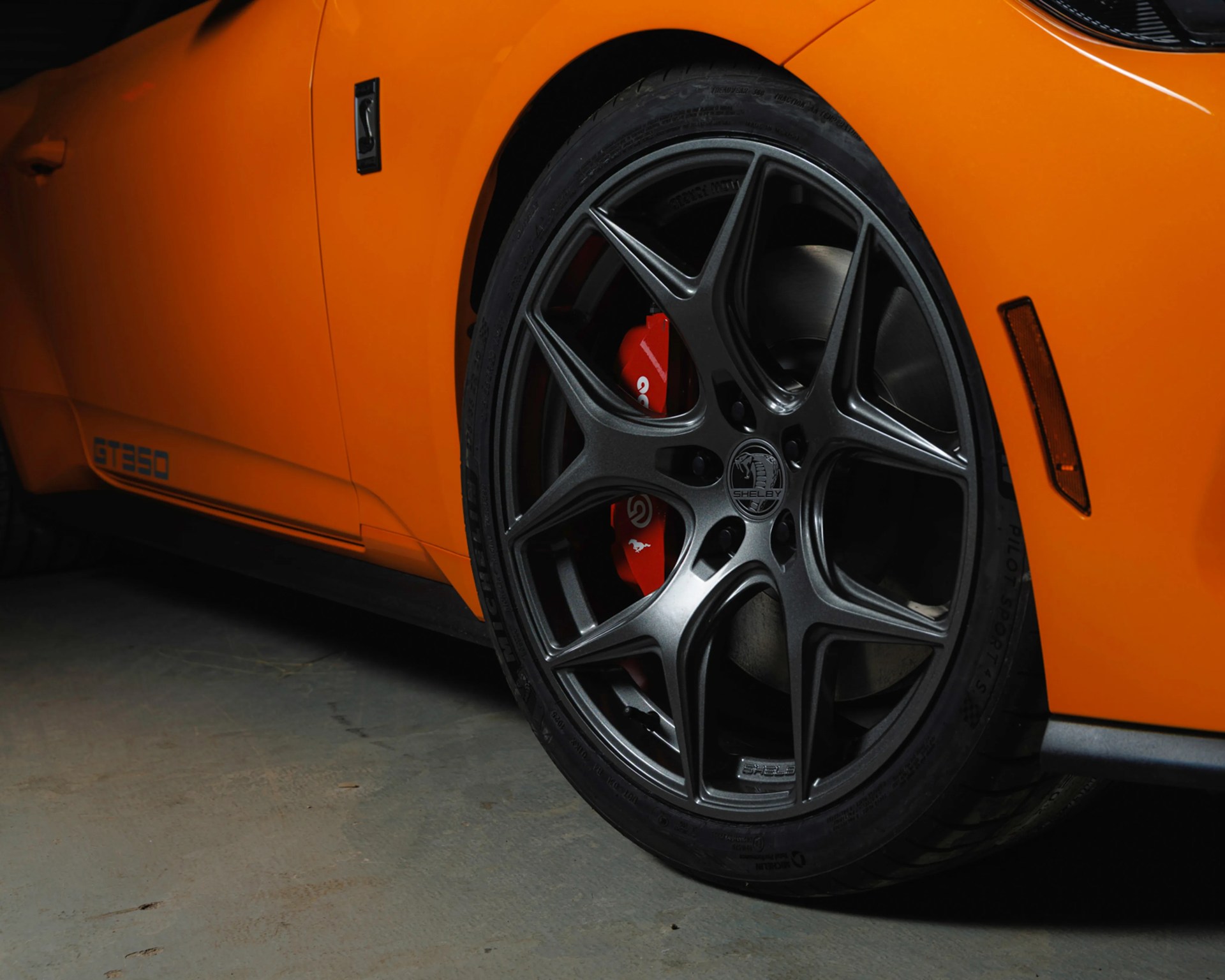 Close-up of a black Shelby alloy wheel with red Brembo brake caliper on an orange GT350 car.