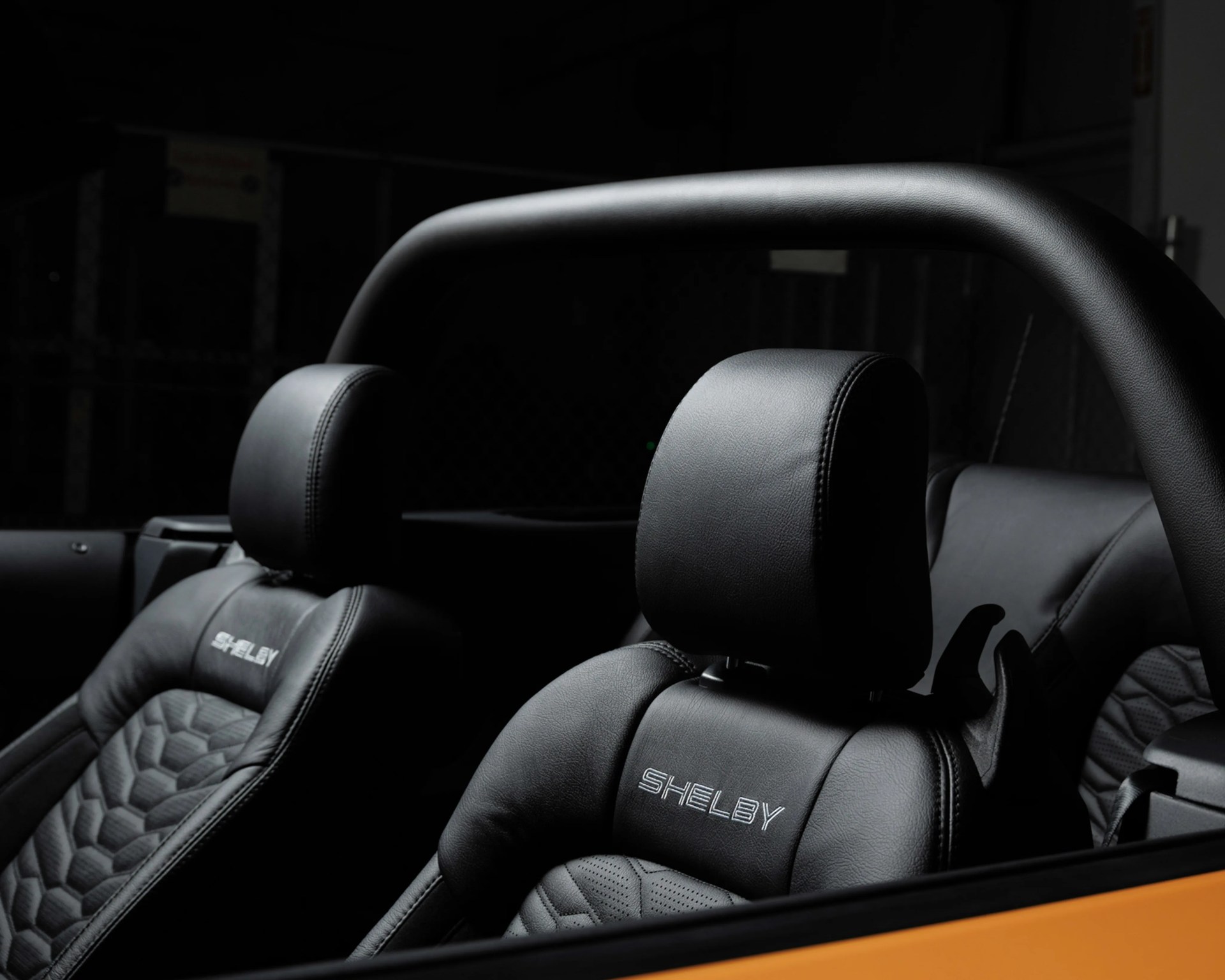 Black leather car seats with "SHELBY" embroidered on the headrests inside a vehicle with a roll bar.