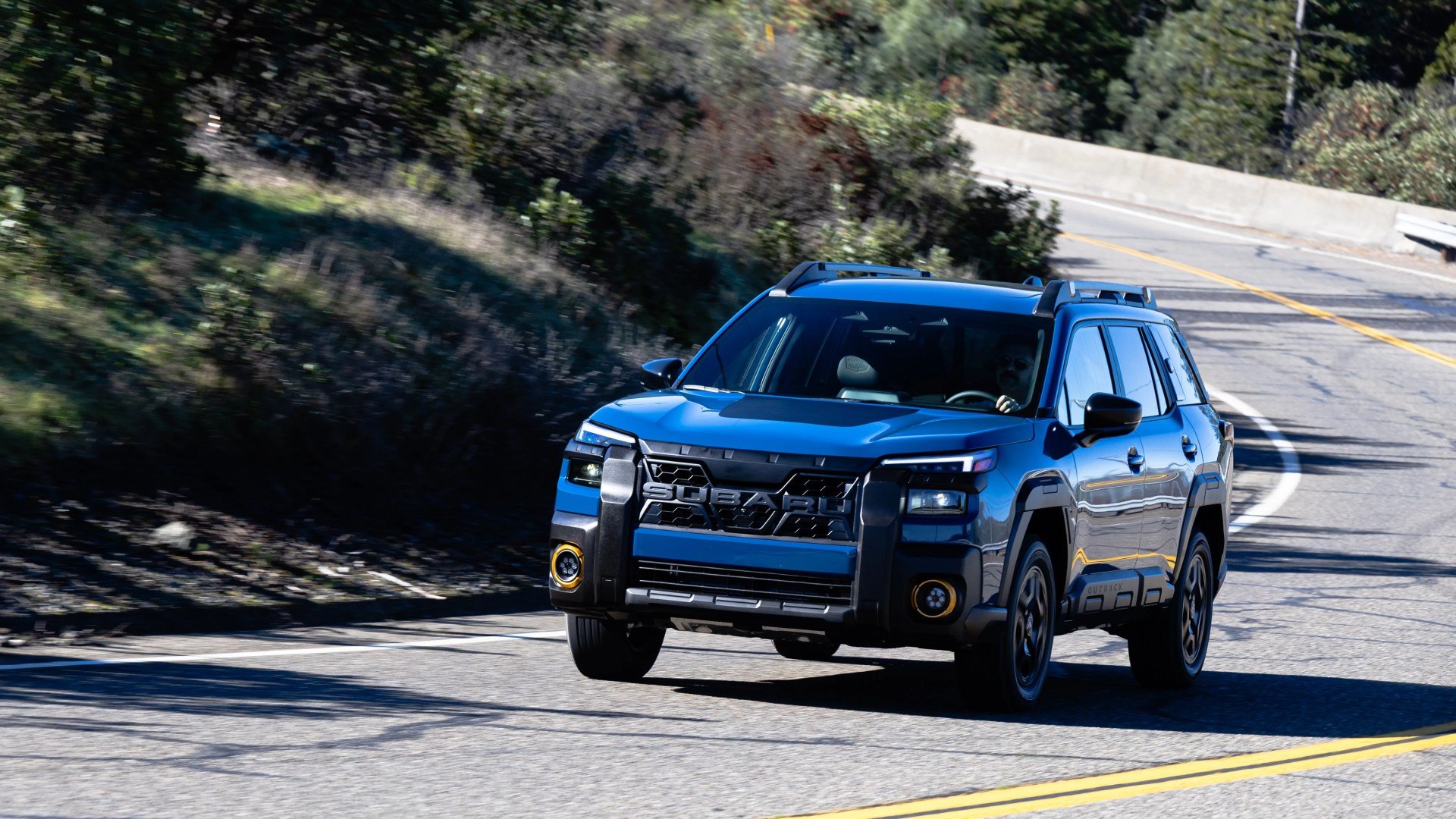 Blue Subaru SUV with black trim driving on a winding mountain road.