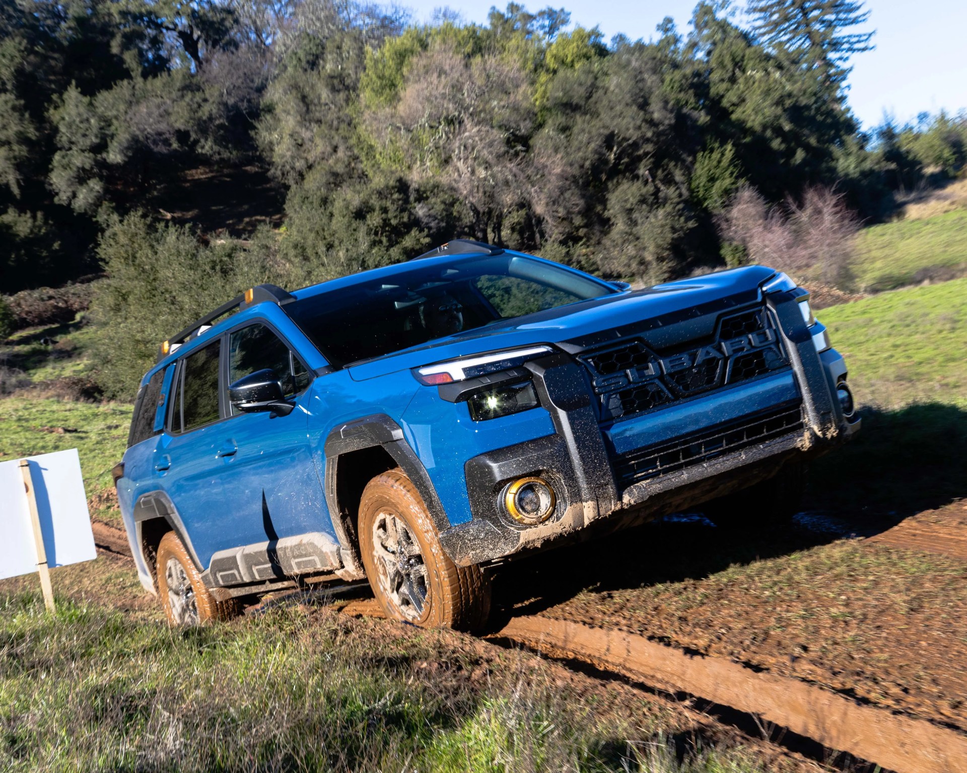 Blue Subaru SUV with mud on tires and lower body driving off-road on a dirt trail.