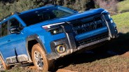 Blue Subaru SUV with mud-covered tires driving off-road on a grassy dirt path.
