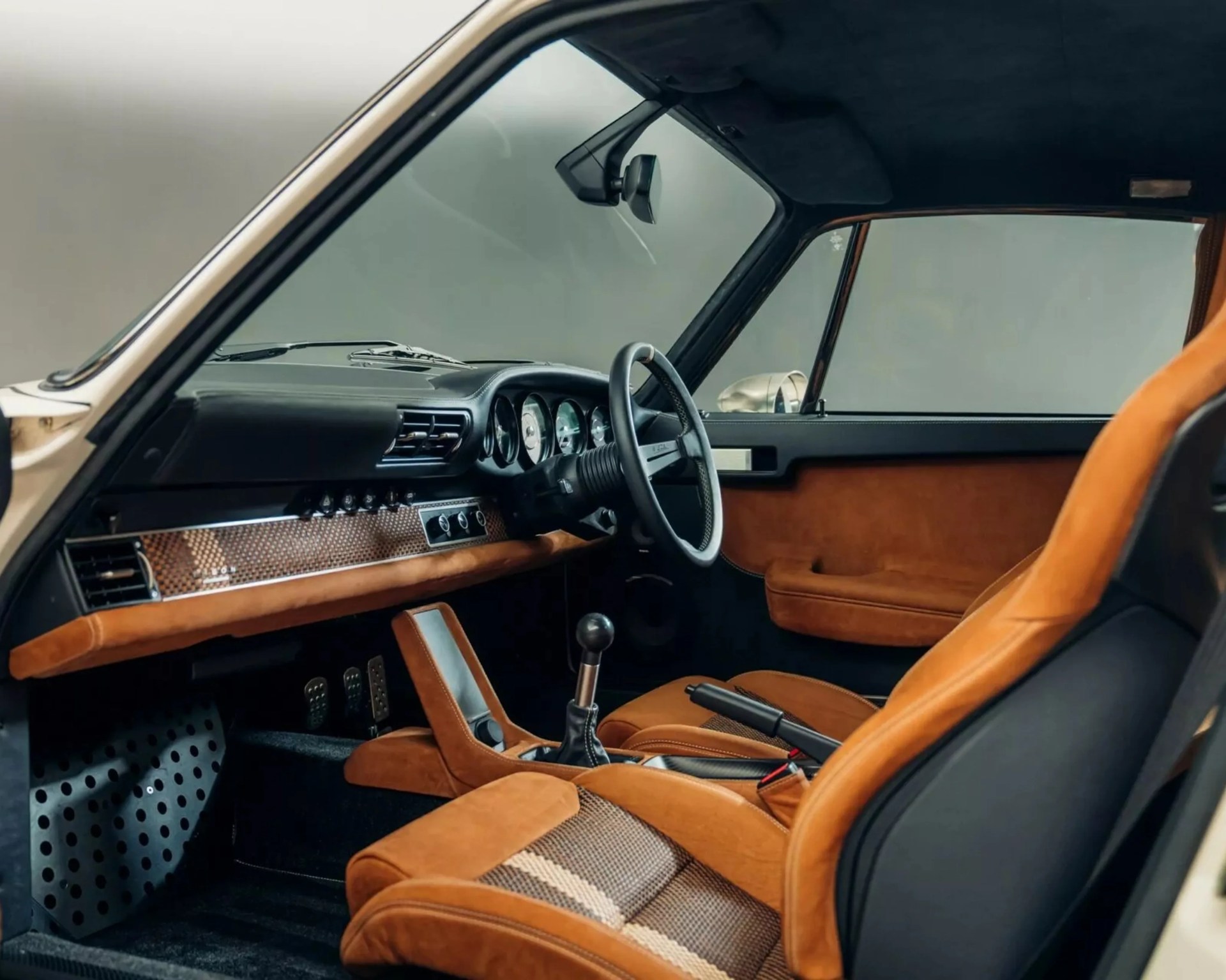 Vintage car interior with tan suede and patterned fabric seats, black dashboard, and manual gear shift.