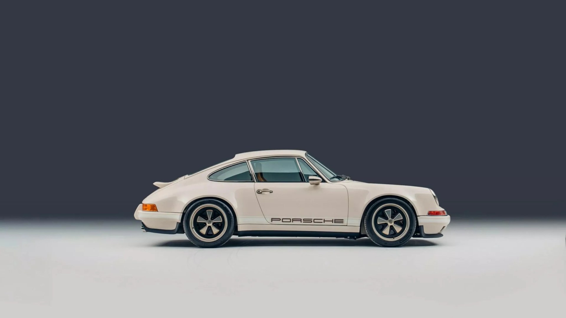 White vintage Porsche 911 with black "Porsche" lettering on the side, shown in profile on a gray background.