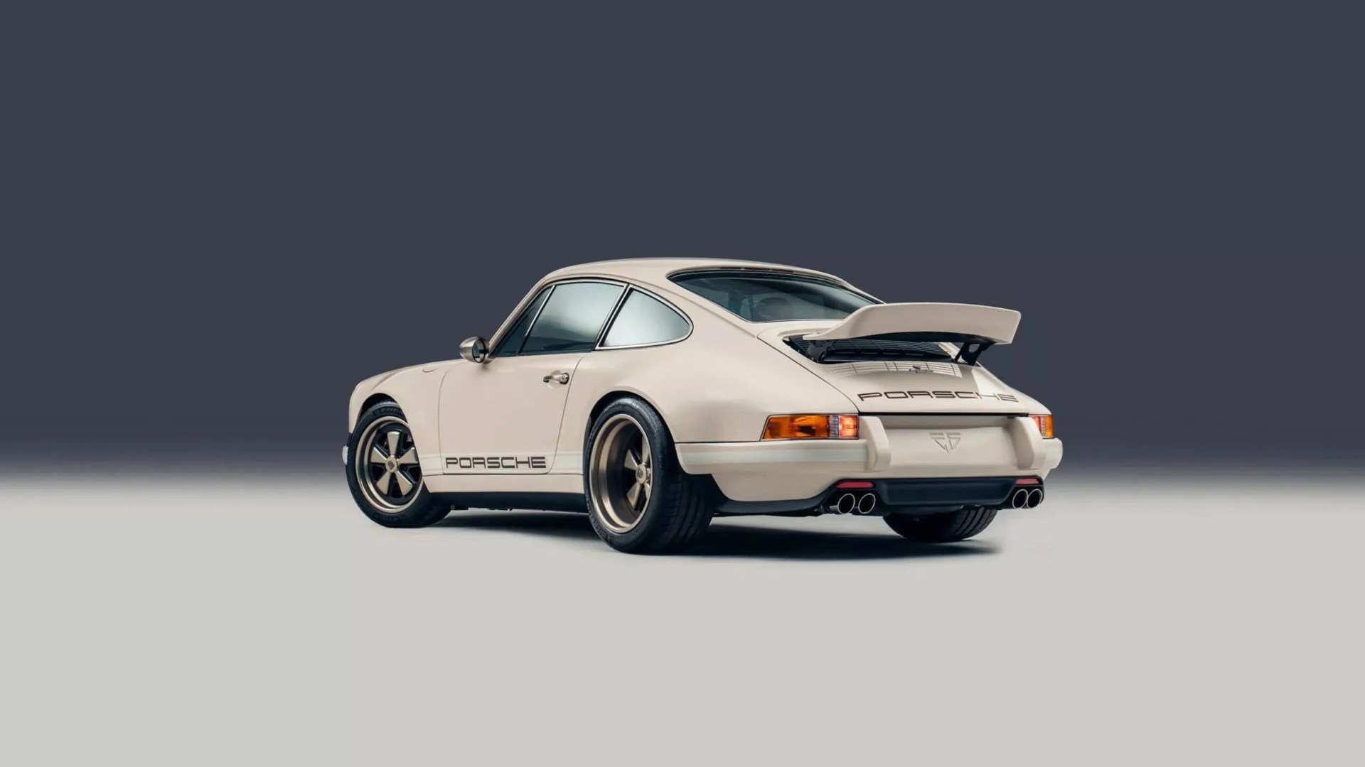 Cream-colored classic Porsche 911 with rear spoiler and bronze wheels on a two-tone gray background.