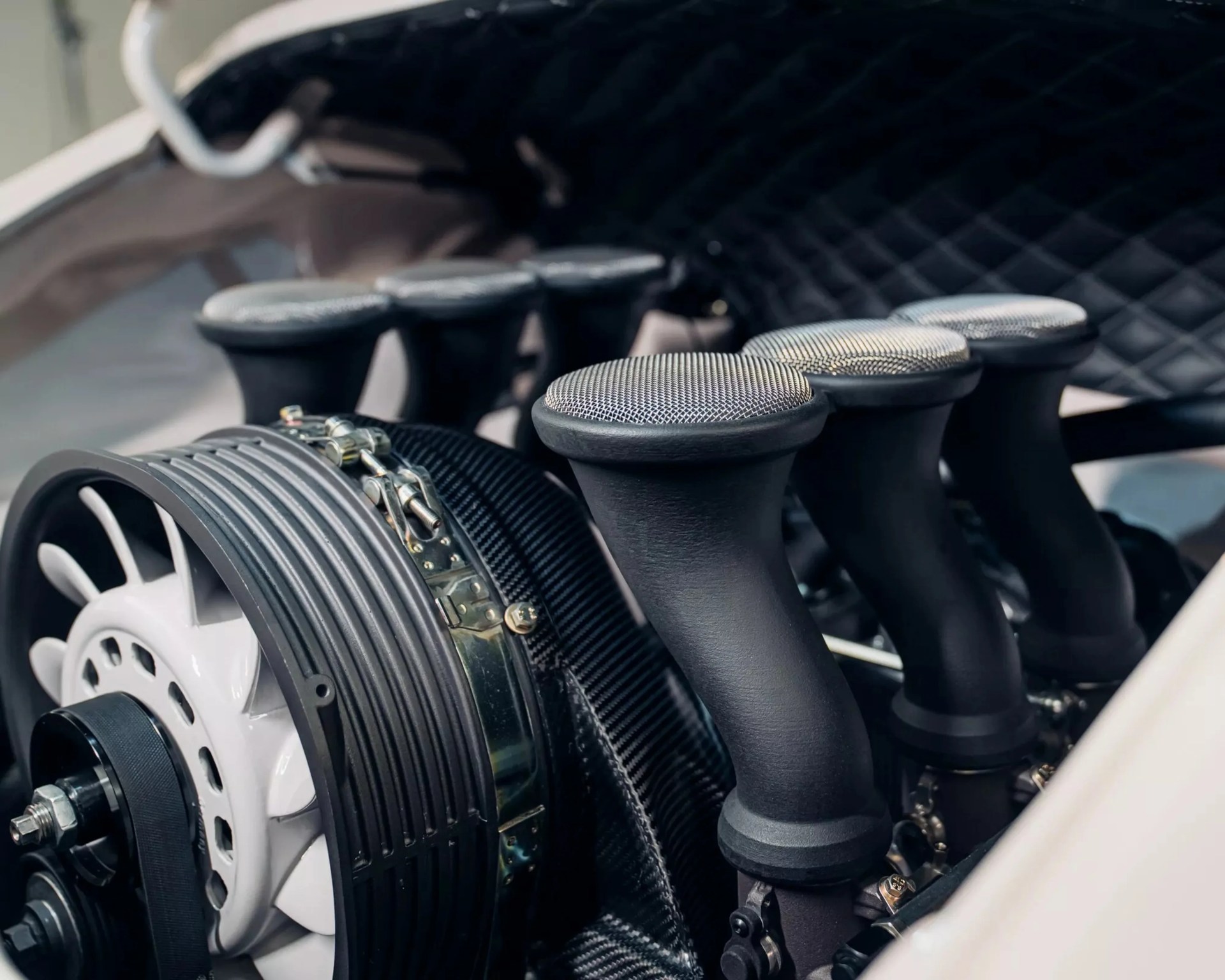 Close-up of a car engine intake system with black velocity stacks and a white cooling fan.