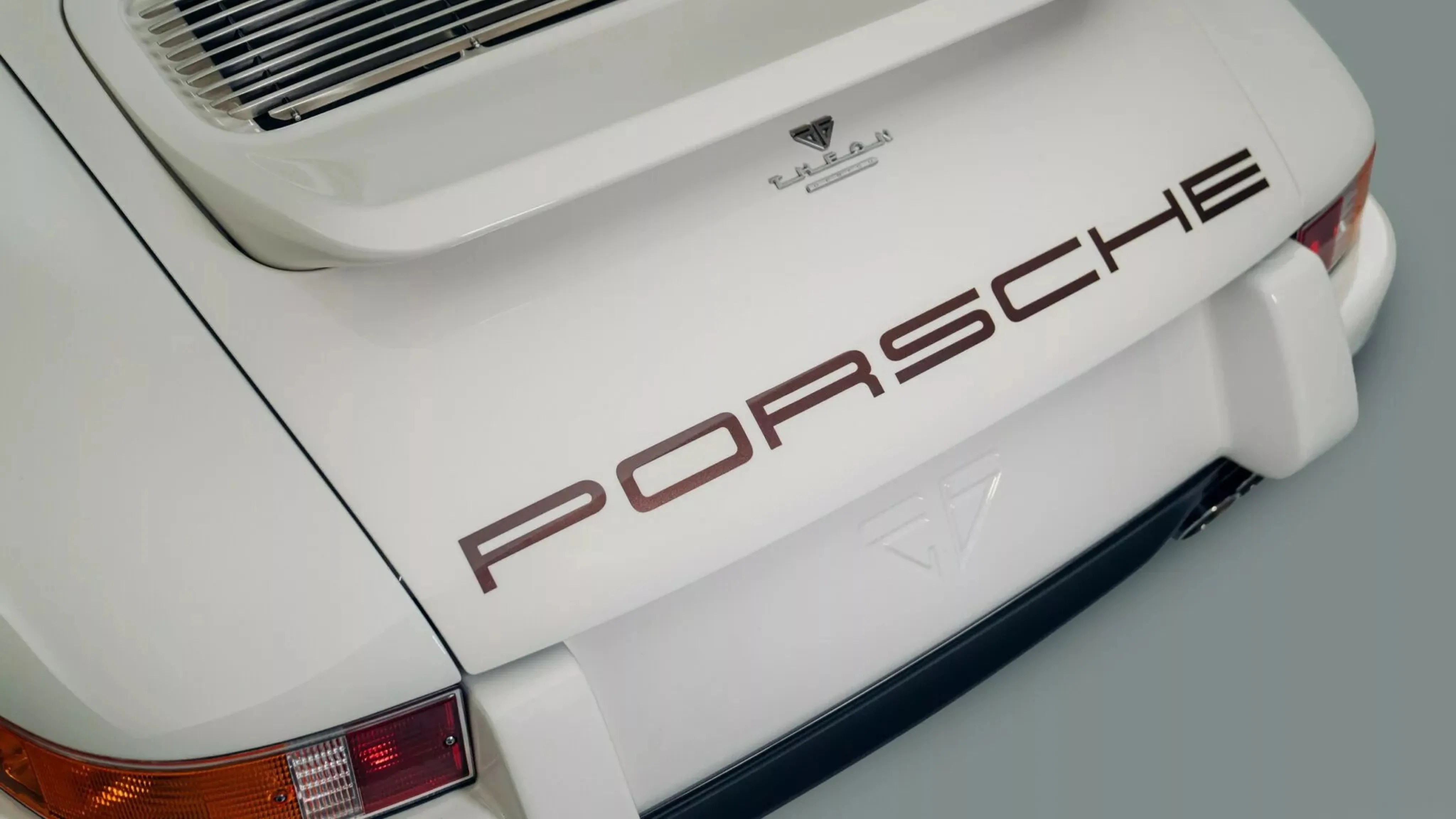 Rear view of a white Porsche car with brown "PORSCHE" lettering and a rear spoiler.