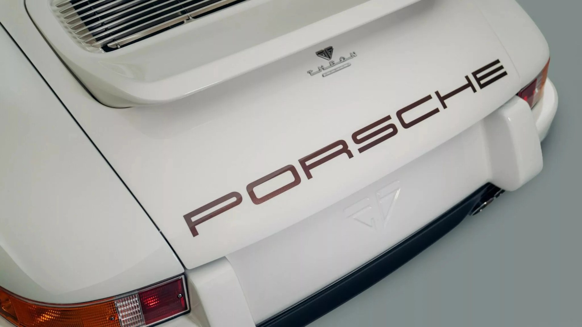 Rear view of a white Porsche car with brown "PORSCHE" lettering and a rear spoiler.