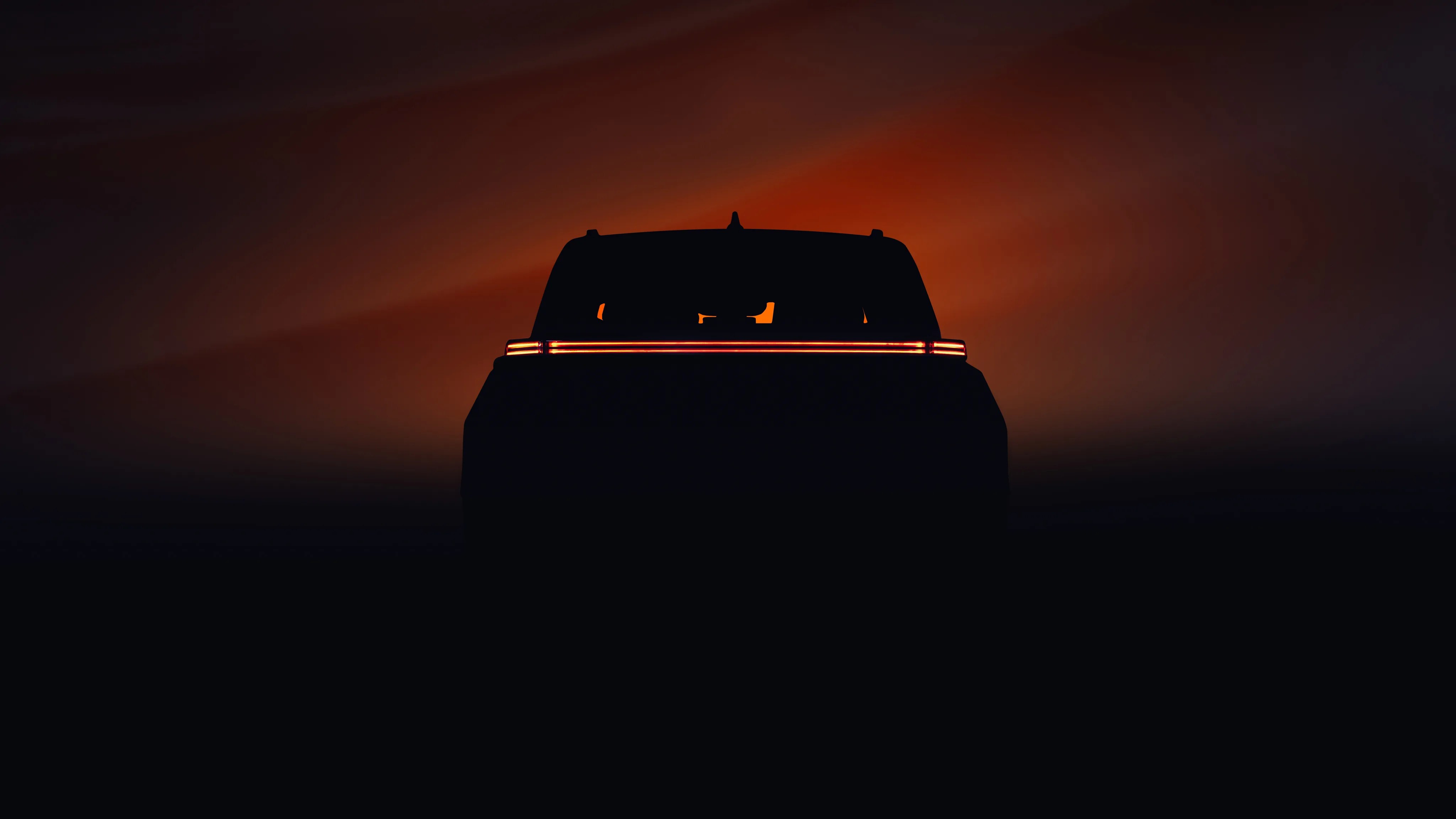 Silhouette of a vehicle rear with a continuous horizontal red taillight strip against a dark orange background.