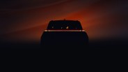 Silhouette of a vehicle rear with a continuous horizontal red taillight strip against a dark orange background.