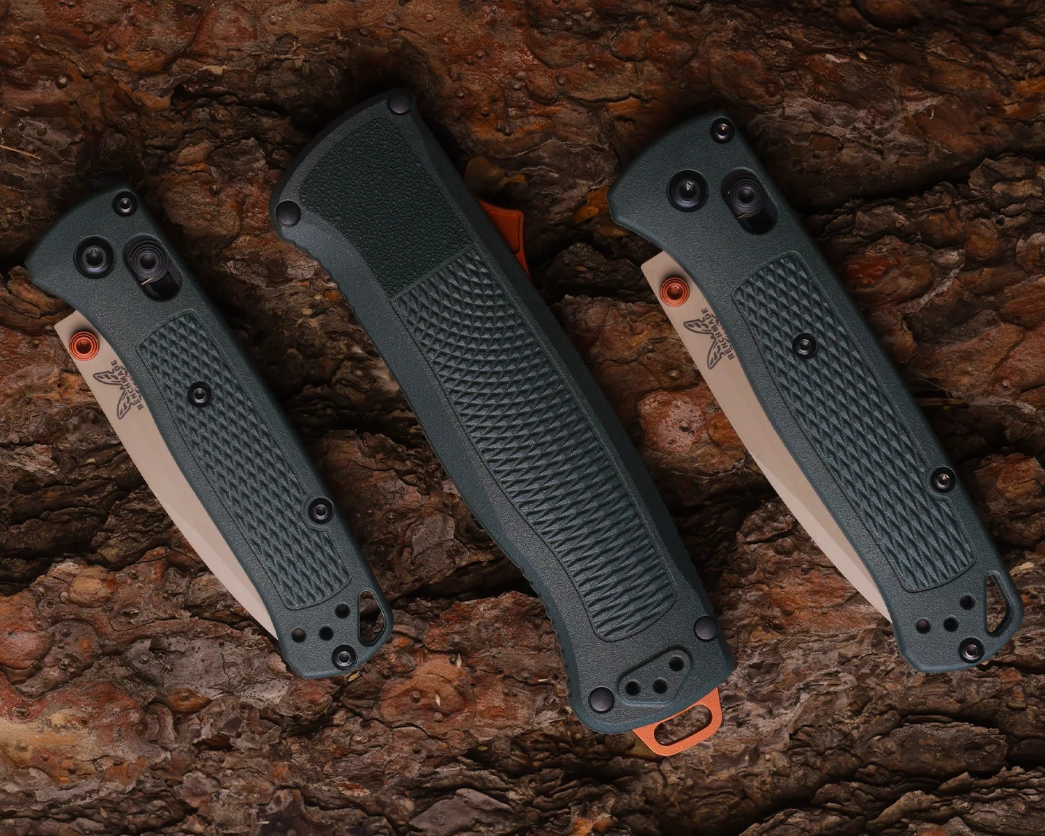 Three closed folding knives with textured dark green handles and partially visible blades on a rough brown bark surface.
