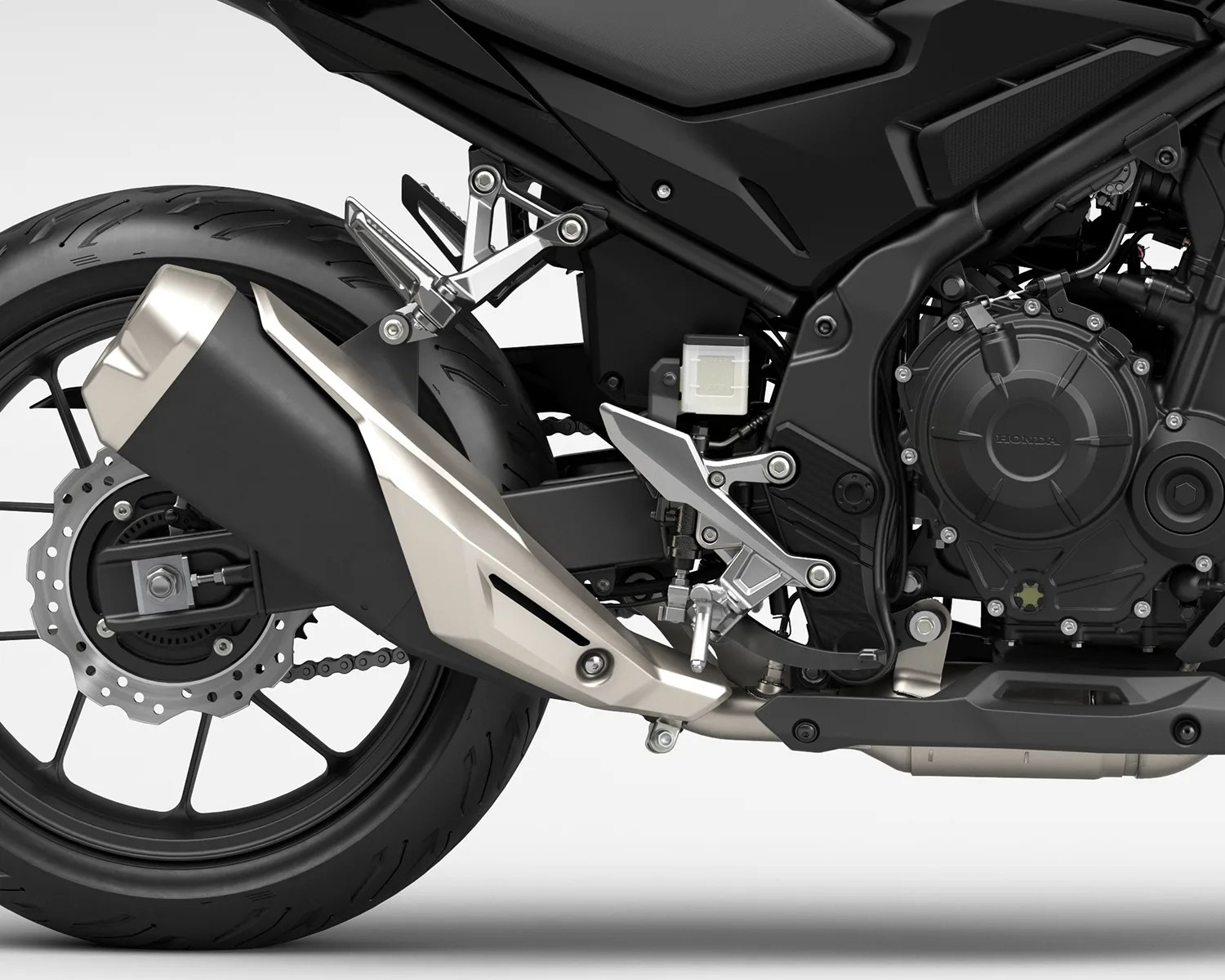 Close-up of a black motorcycle's rear wheel, exhaust pipe, footpeg, and engine casing with visible "Honda" logo.
