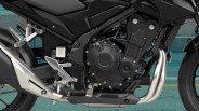 Close-up of a black motorcycle engine with silver exhaust pipes and foot pegs on a teal pavement background.