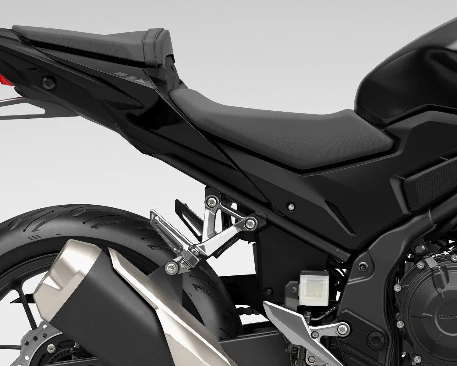 Close-up of the rear section of a black motorcycle showing the seat, exhaust, rear tire, and footpeg assembly.
