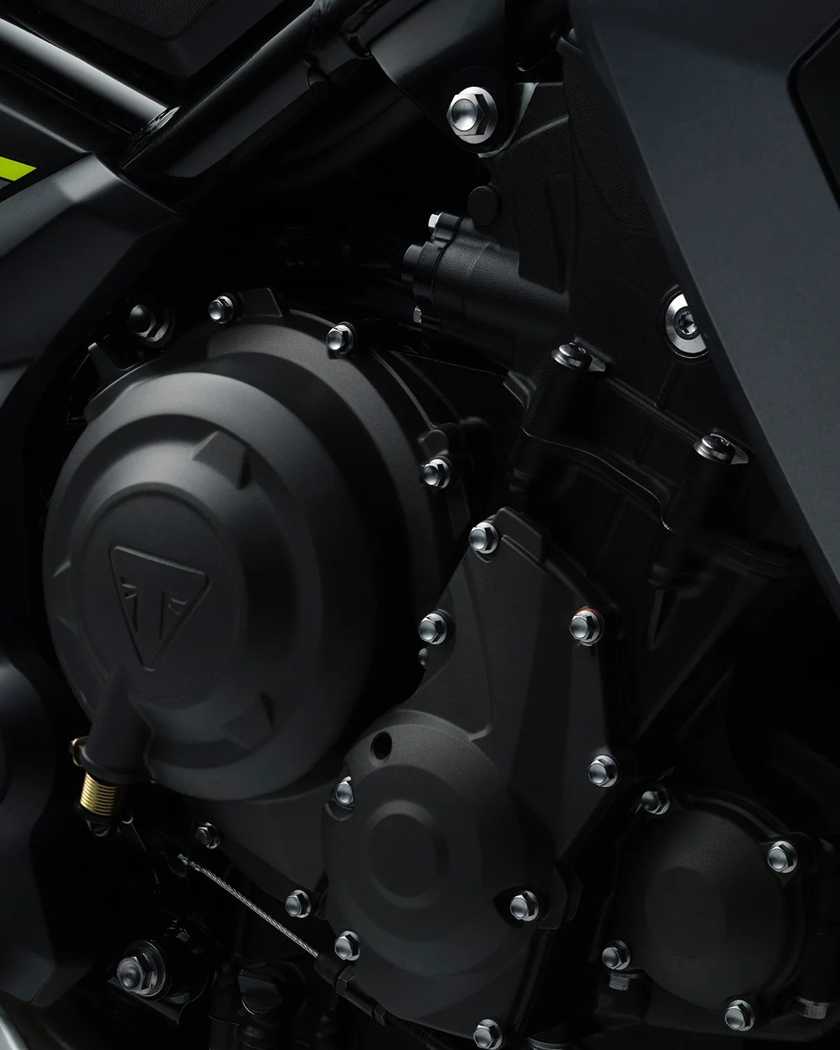 Close-up of a matte black motorcycle engine casing with multiple silver bolts and a triangular logo embossed on the largest cover.