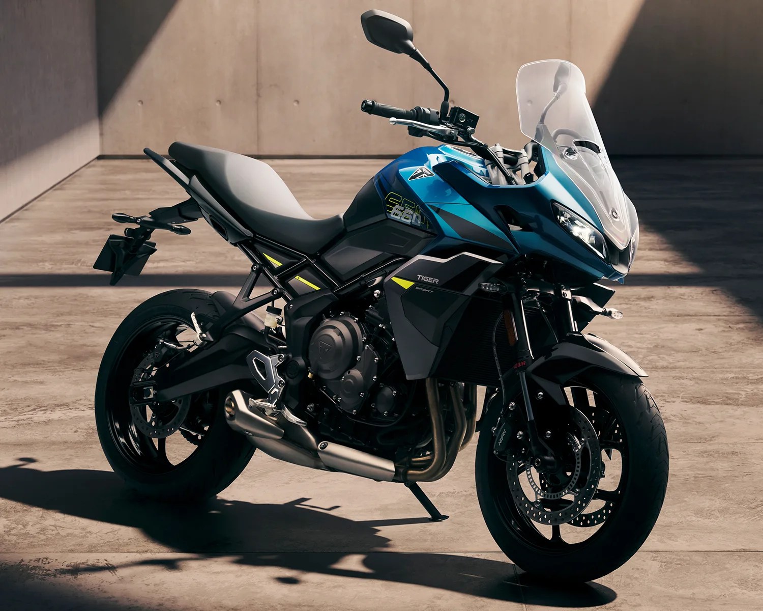 Blue and black Triumph Tiger 660 sport motorcycle with windshield on a concrete floor.
