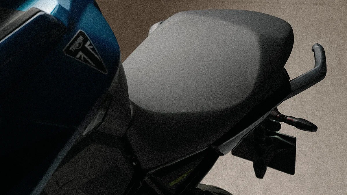 Close-up of a black motorcycle seat with a blue Triumph logo on the adjacent body panel.