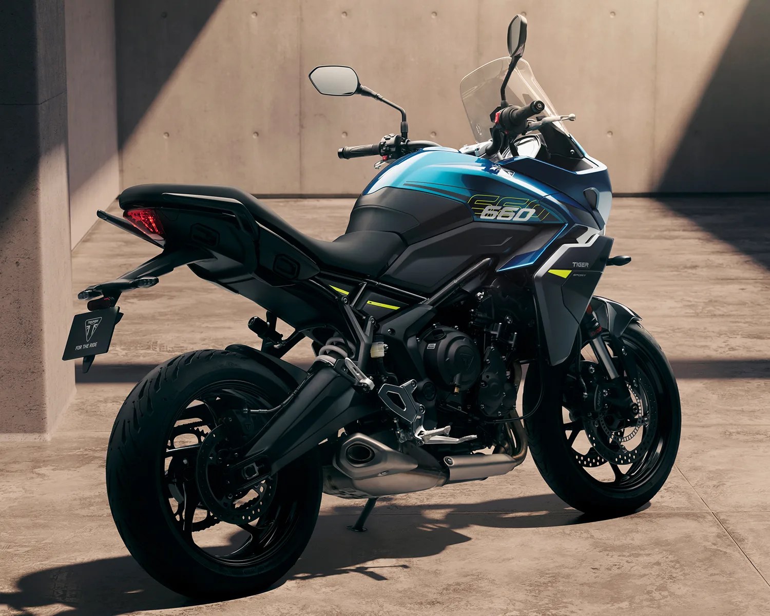 Blue and black Triumph Tiger 660 sport motorcycle parked indoors with concrete walls and floor.