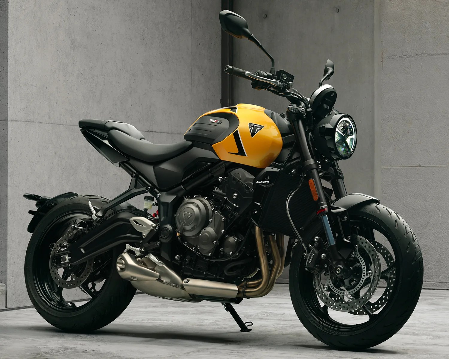 Yellow and black Triumph motorcycle with exposed engine and round headlight on a concrete floor.