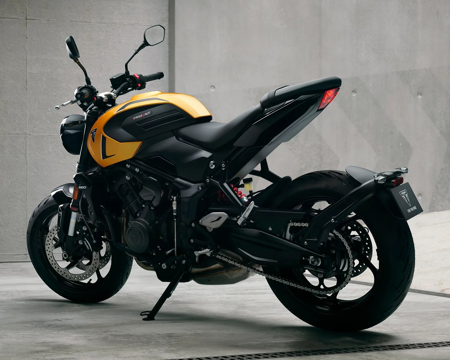 Yellow and black Triumph Trident 660 motorcycle parked on a concrete floor against a gray wall.