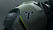 Close-up of a matte green motorcycle fuel tank with black and yellow stripes, featuring Triumph and Trident logos.