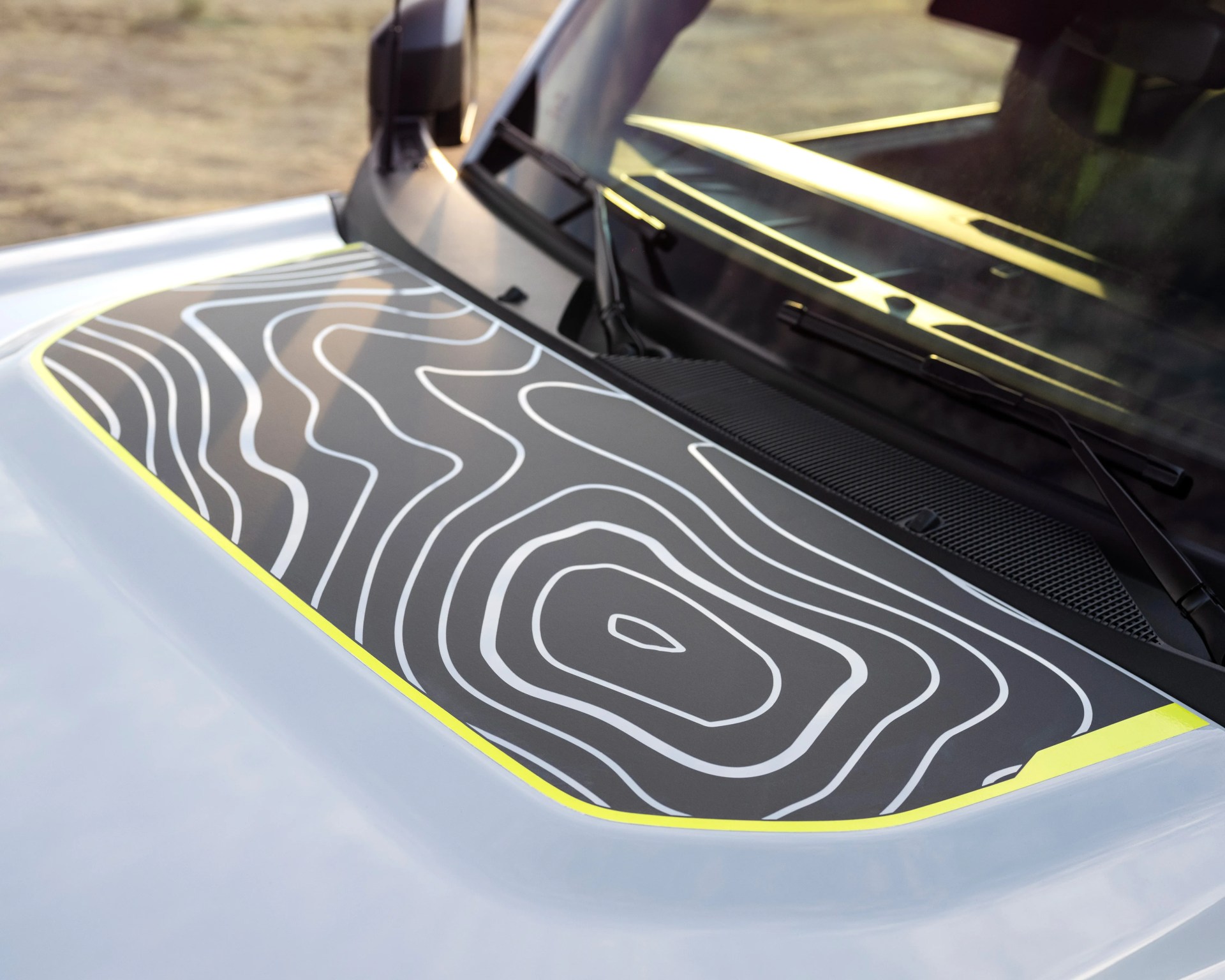 Close-up of a car hood with a black decal featuring white contour lines and a yellow border near the windshield.